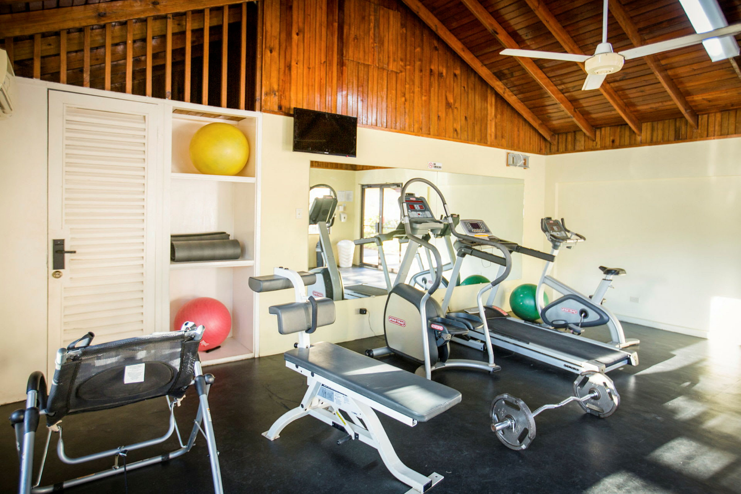 Ett gymrum med träningsutrustning som crosstrainers, träningsbänk och pilatesbollar. (AI-genererad text)