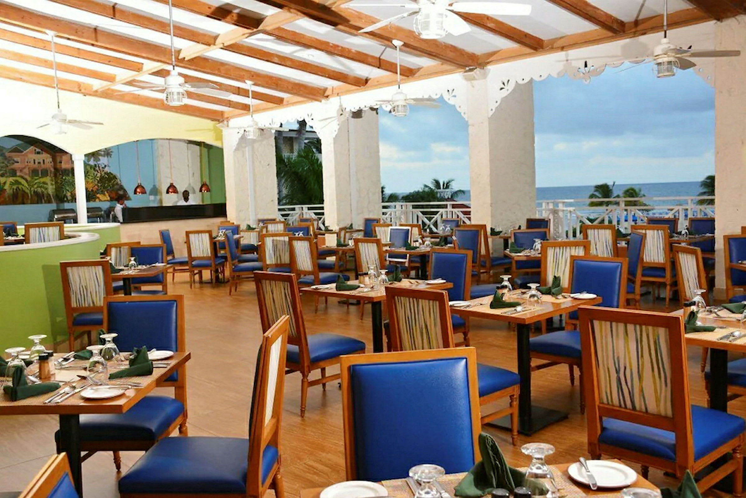 Restaurang med trästolar av blå sits och dukade bord med havsutsikt. (AI-genererad text)