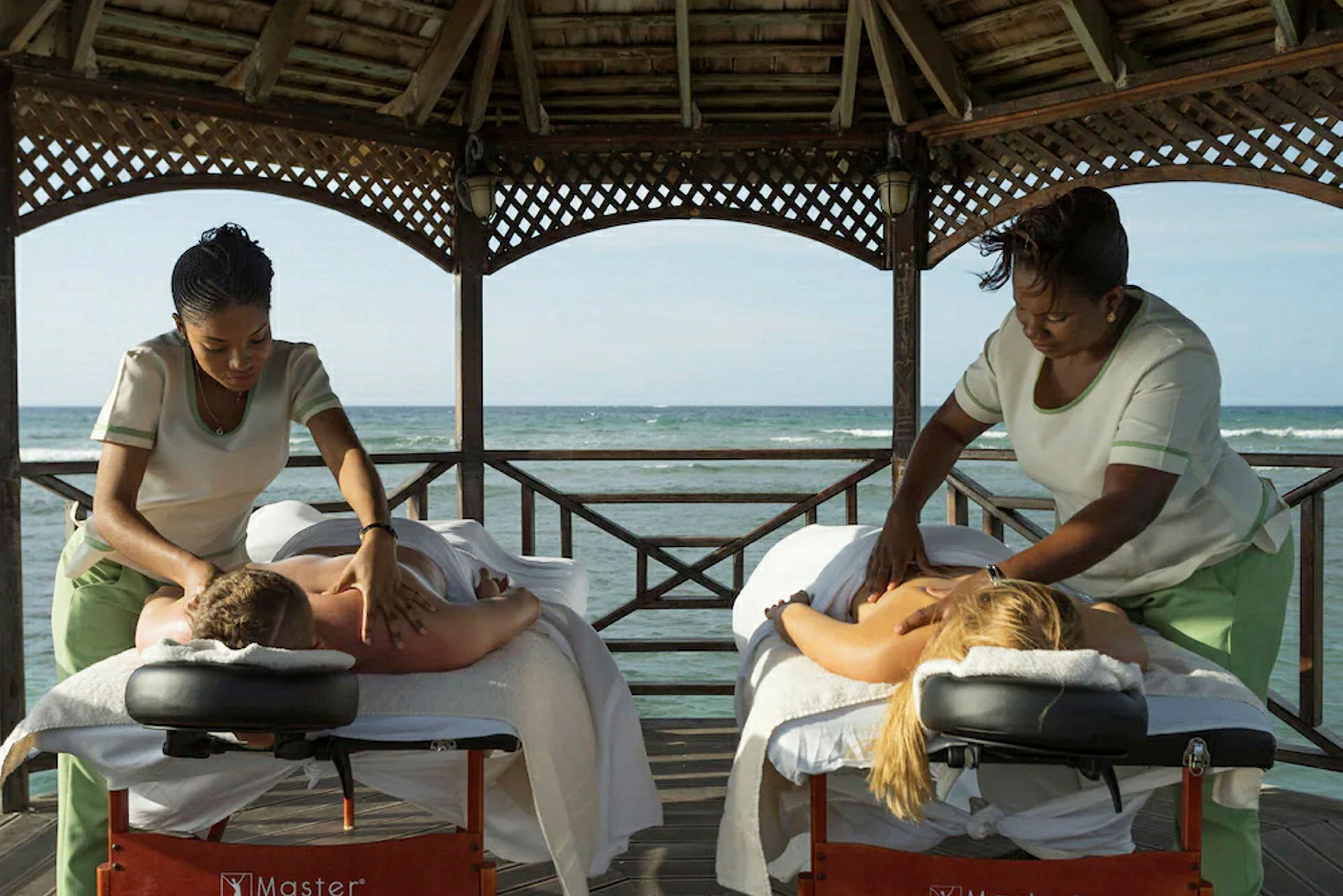 Två personer får massage under ett tak på en brygga med havet i bakgrunden. (AI-genererad text)