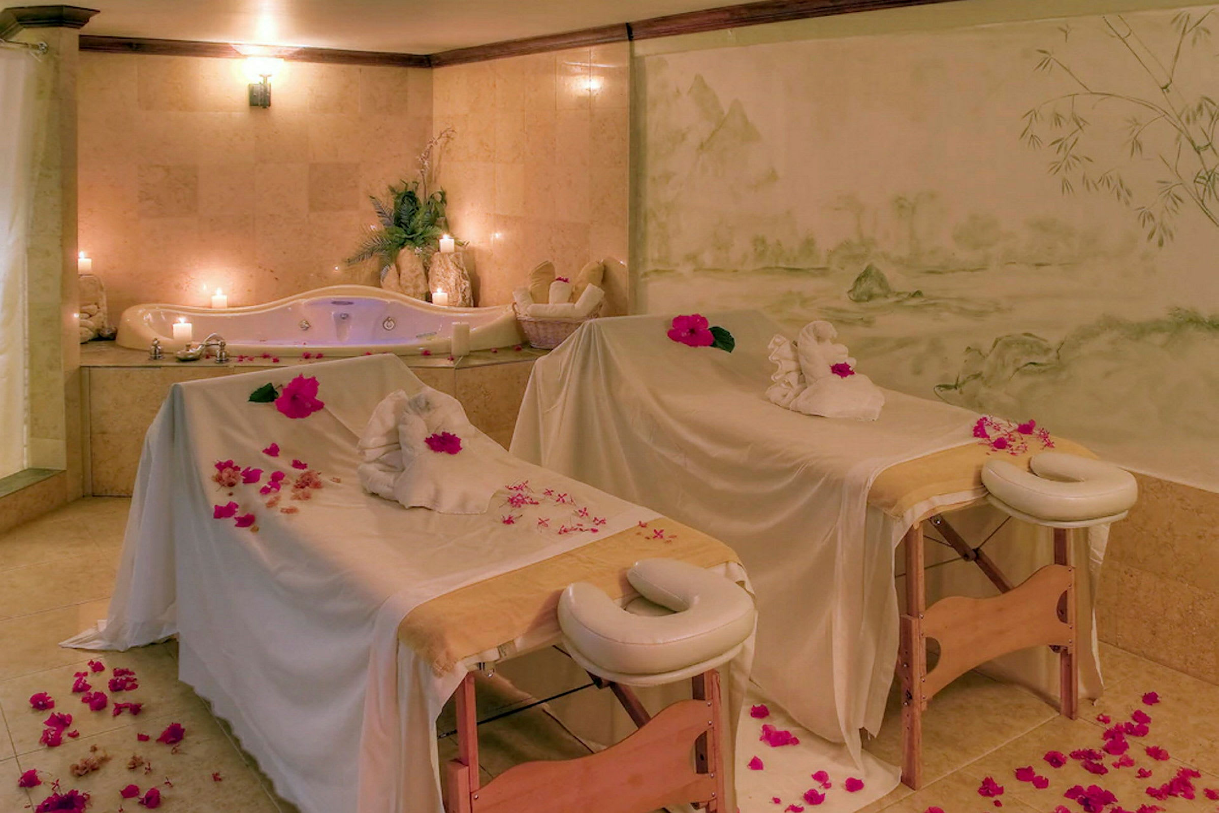 Bild på ett spa med två massagebänkar, en jacuzzi och tända ljus. (AI-genererad text)