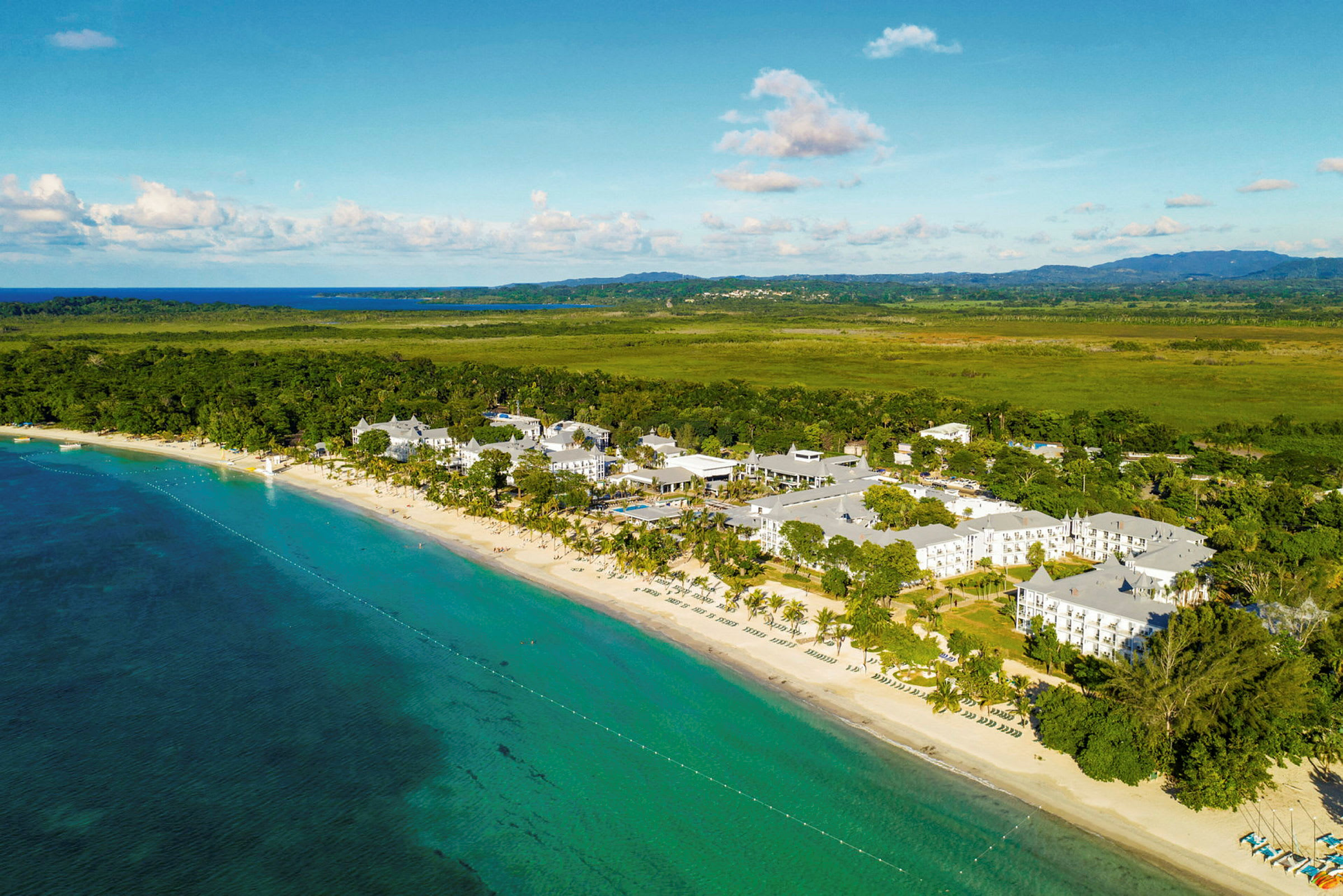 Flygfoto över en strand vid ett turkost hav och ett hotellkomplex omgivna av frodig grönska. (AI-genererad text)
