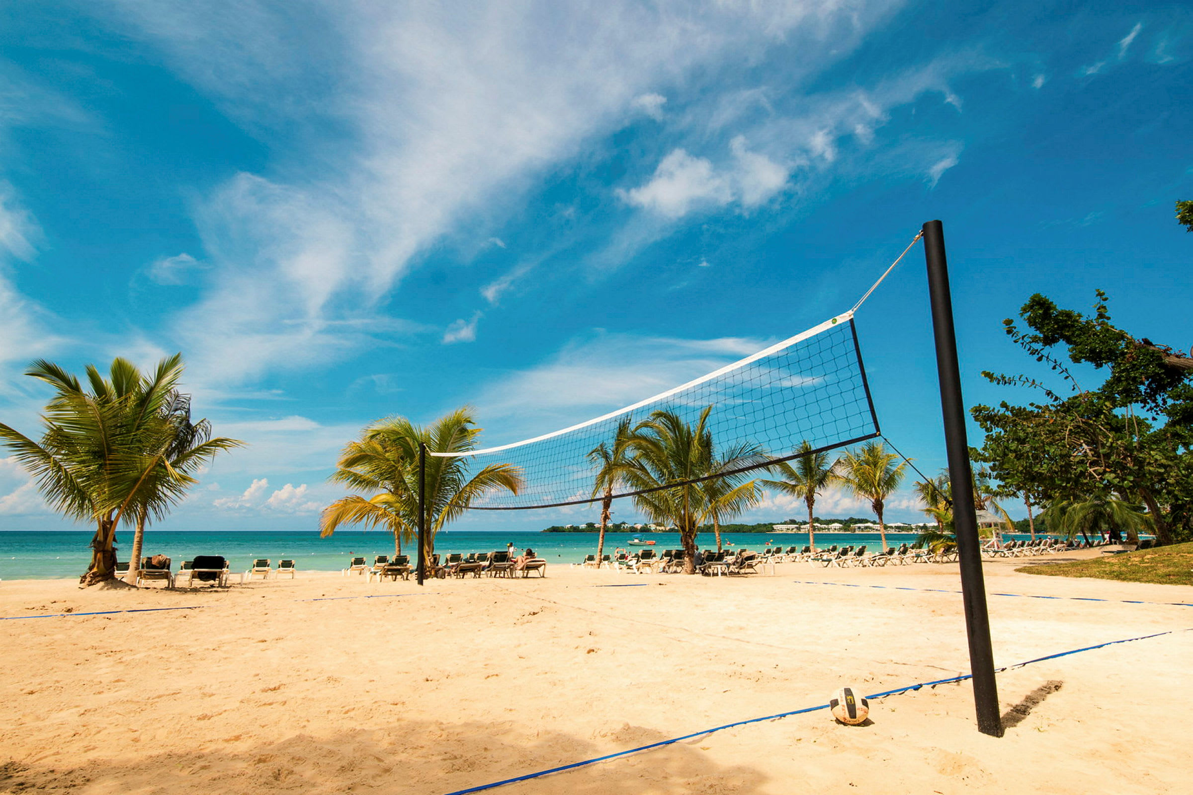 En strand med ett volleybollnät, sand och palmer i en tropisk miljö. (AI-genererad text)