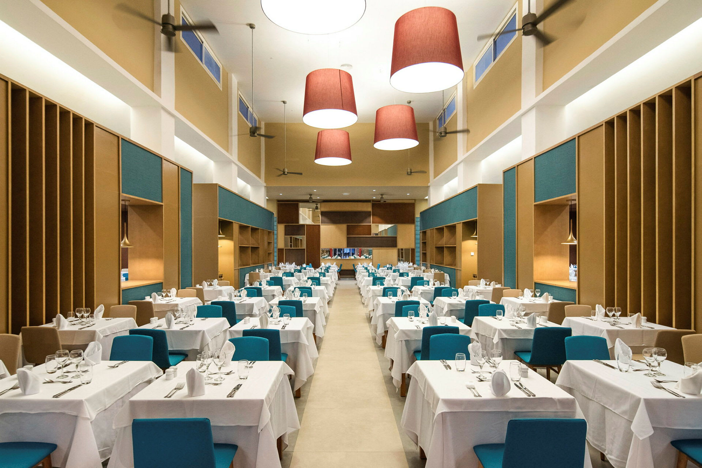 En stor och rymlig restaurang med bord klädda i vita dukar och blåa stolar. (AI-genererad text)