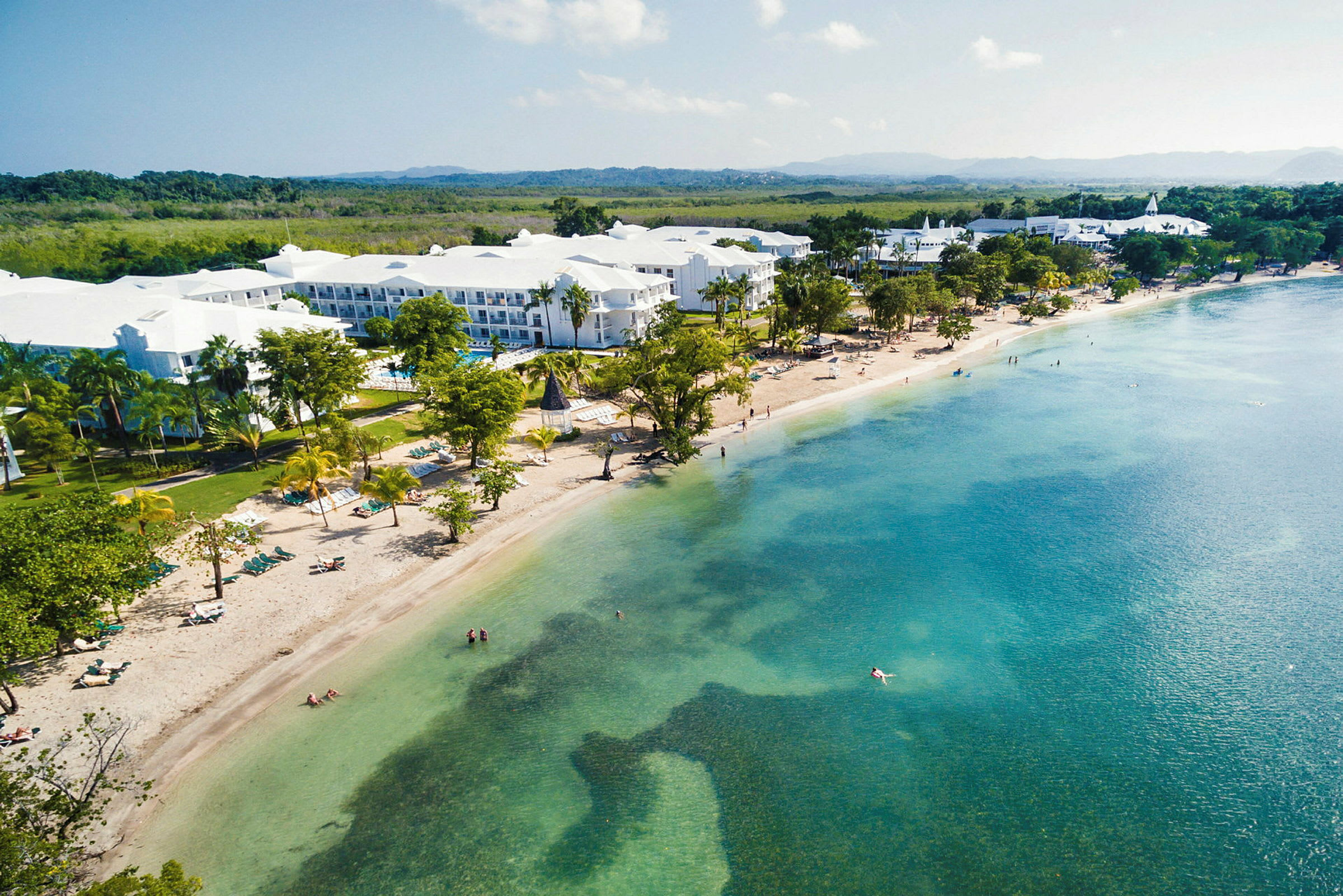 Bild av en strand med klarblått vatten och hotellbyggnader i bakgrunden. (AI-genererad text)