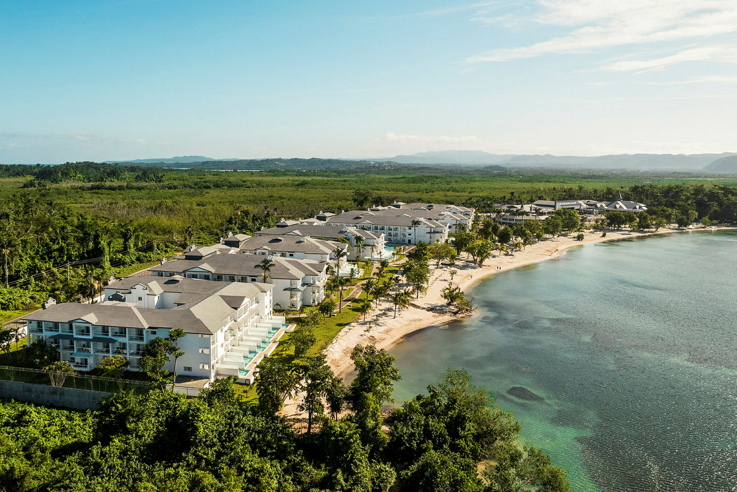 Ett strandområde med resortbyggnader omgivna av grönska och hav. (AI-genererad text)