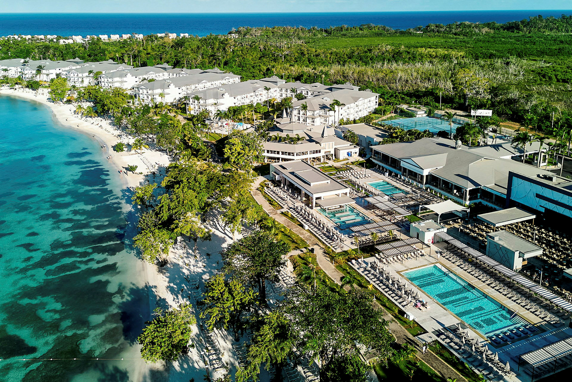 Flygvy över hotellkomplex vid stranden med pooler och omgivande grönska. (AI-genererad text)