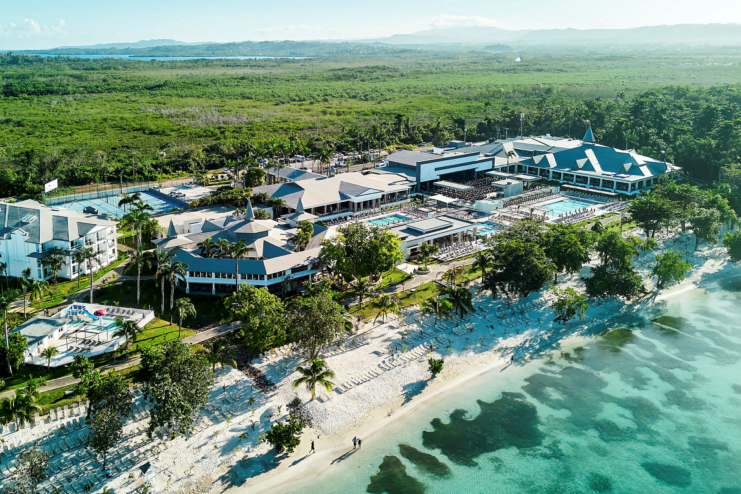 Flygfoto över en resort vid stranden med poolområden och omkringliggande grönska. (AI-genererad text)