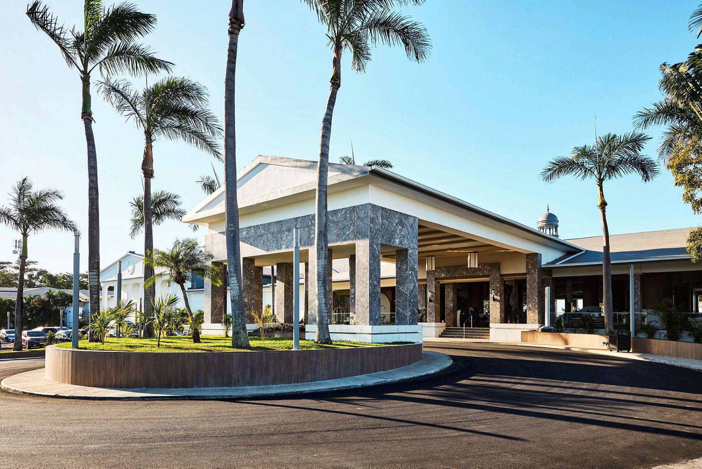 Hotellentré med palmträd och parkeringsplats. (AI-genererad text)