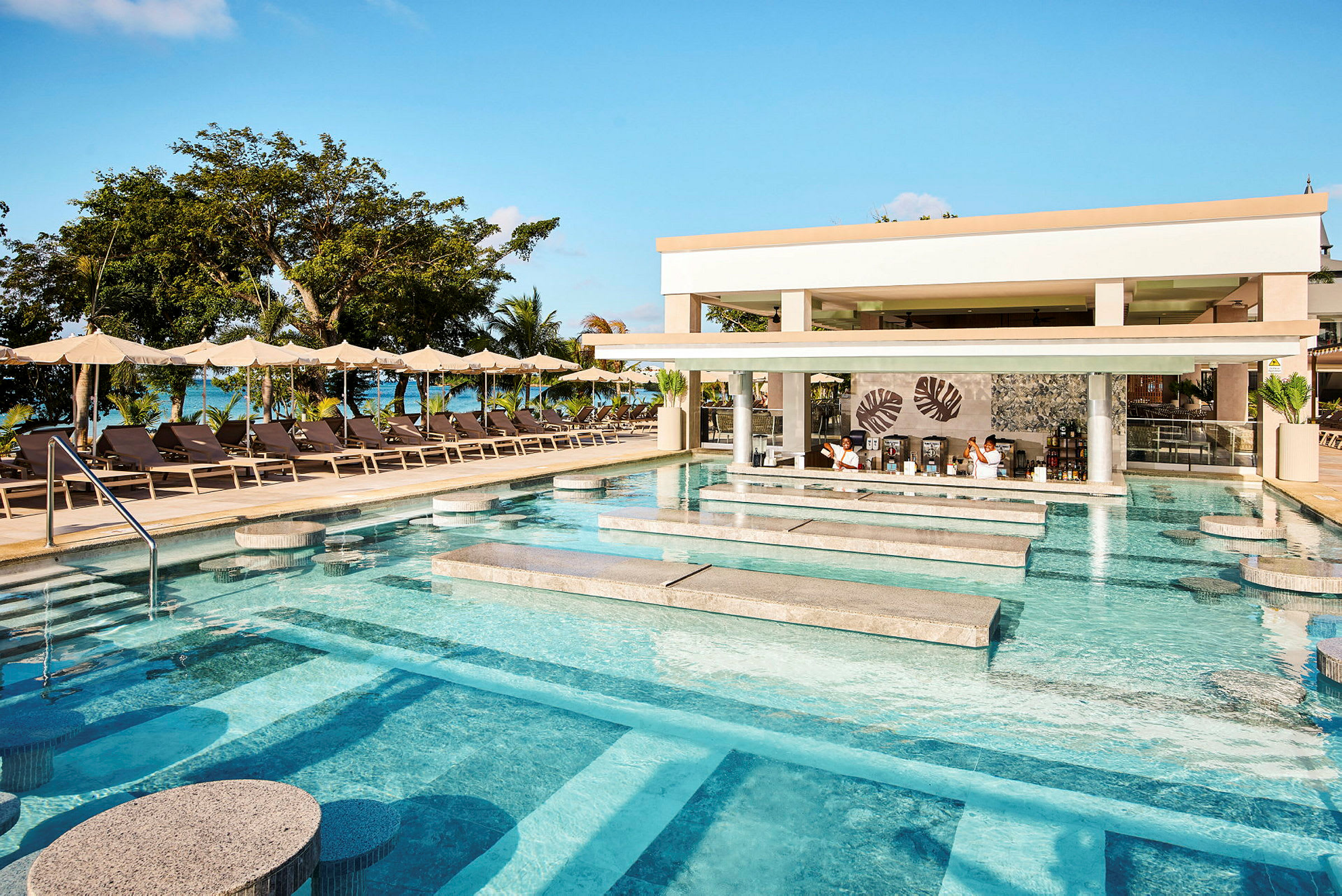 En pool med sittplatser och en swim-up bar vid en resort med solstolar och parasoller i bakgrunden. (AI-genererad text)