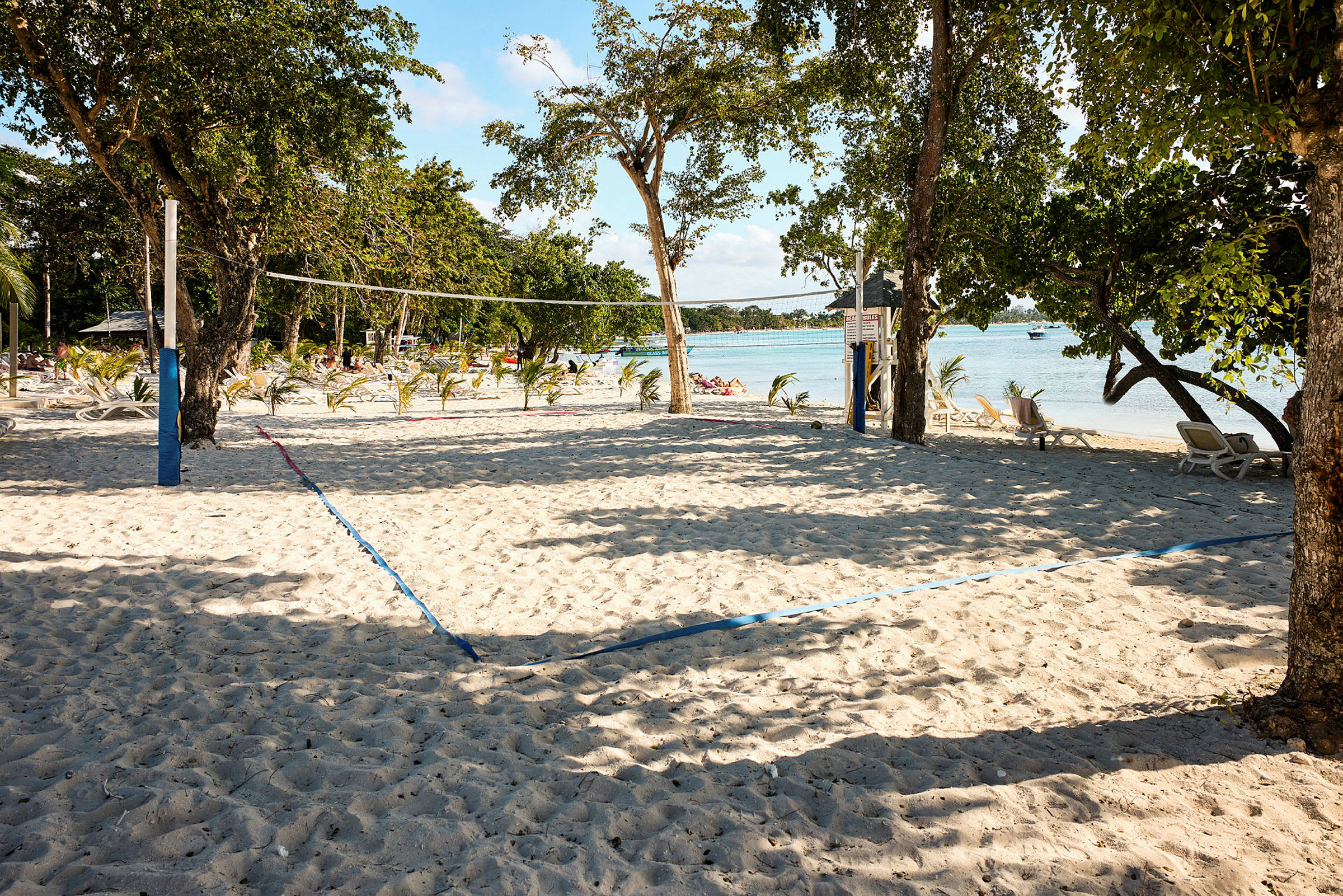 En sandstrand med volleybollnät och stolar i bakgrunden. (AI-genererad text)