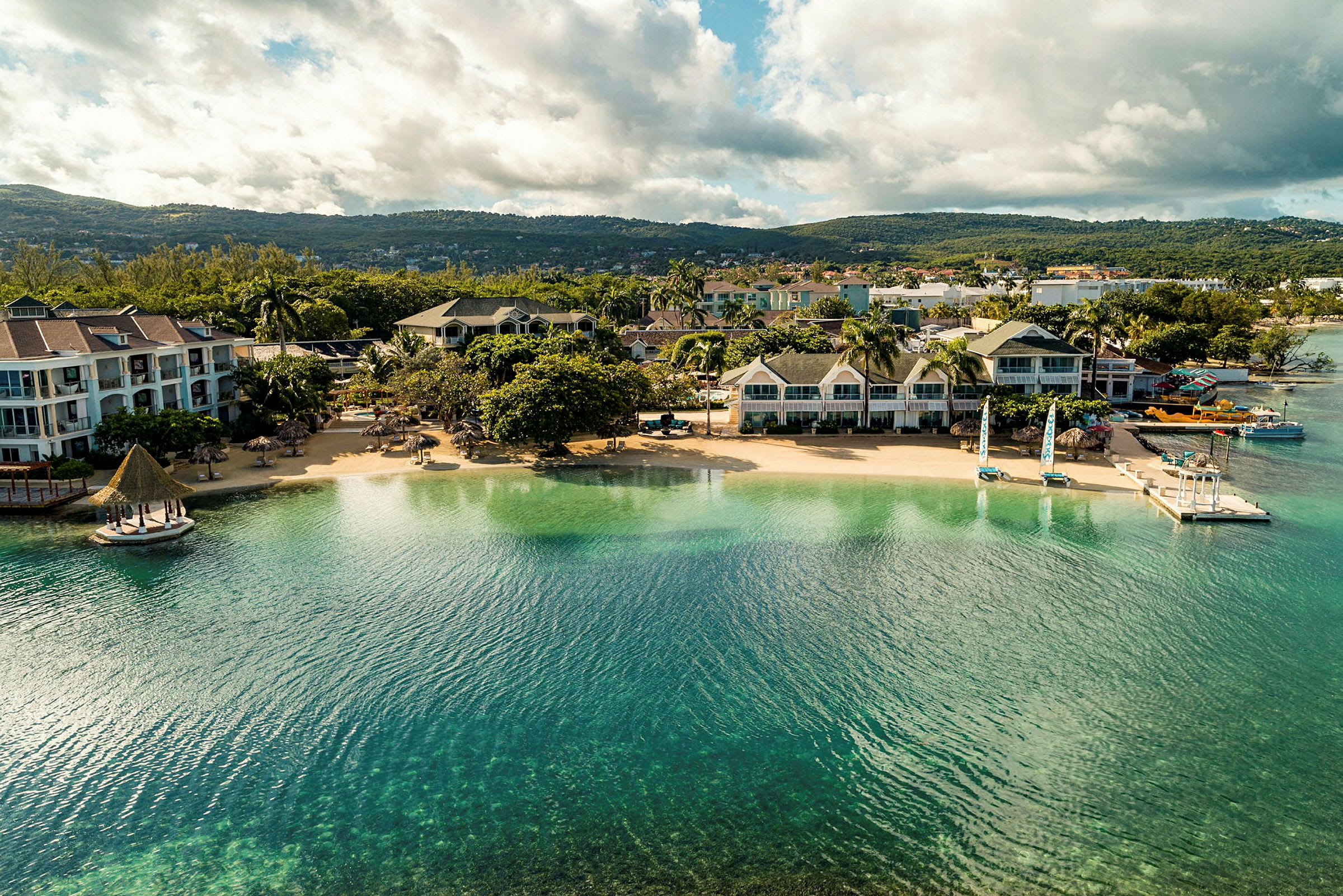 Flygbild av en strand med hotellbyggnader och grönska. (AI-genererad text)
