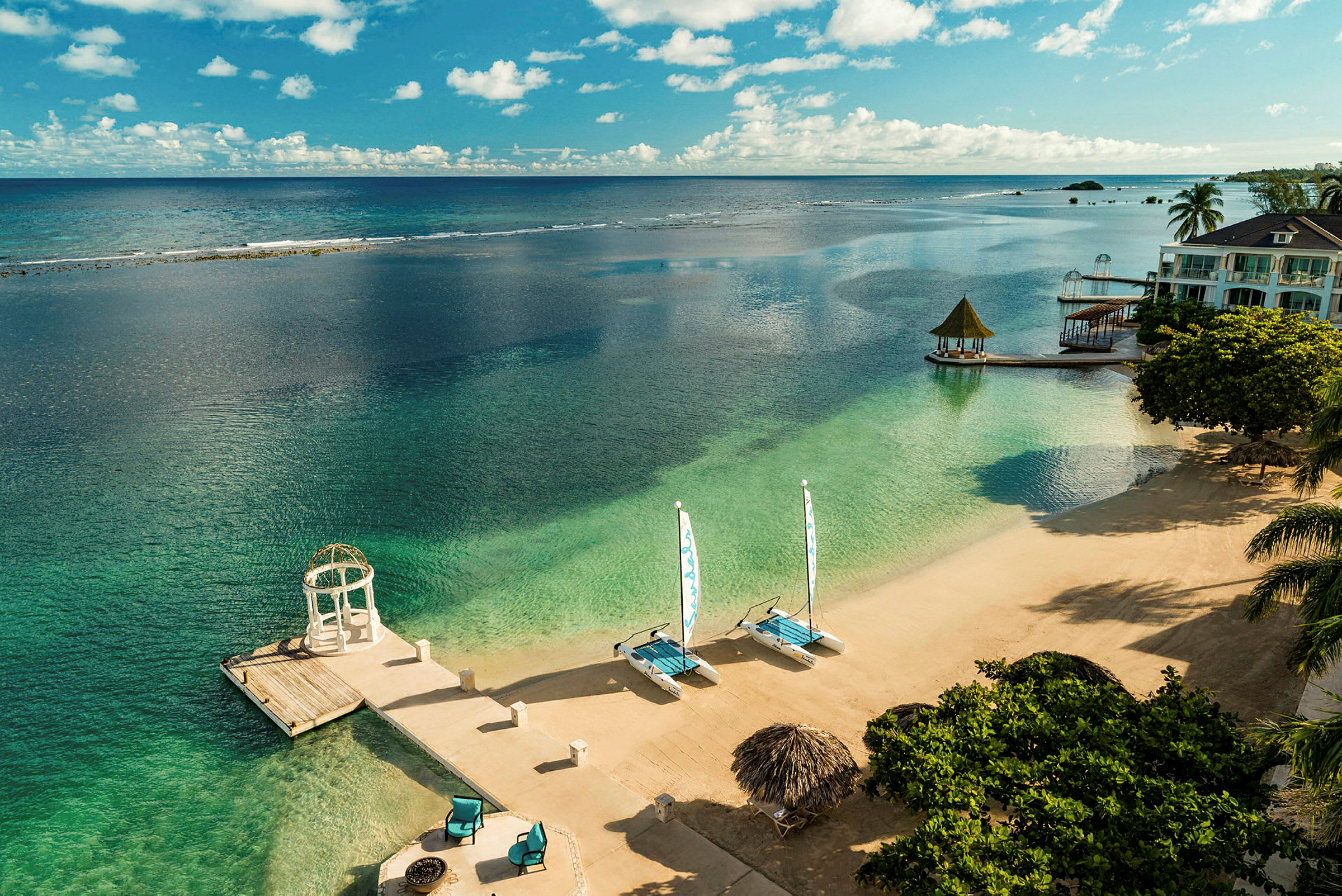 Strand med klart vatten, solstolar och segelbåtar. (AI-genererad text)