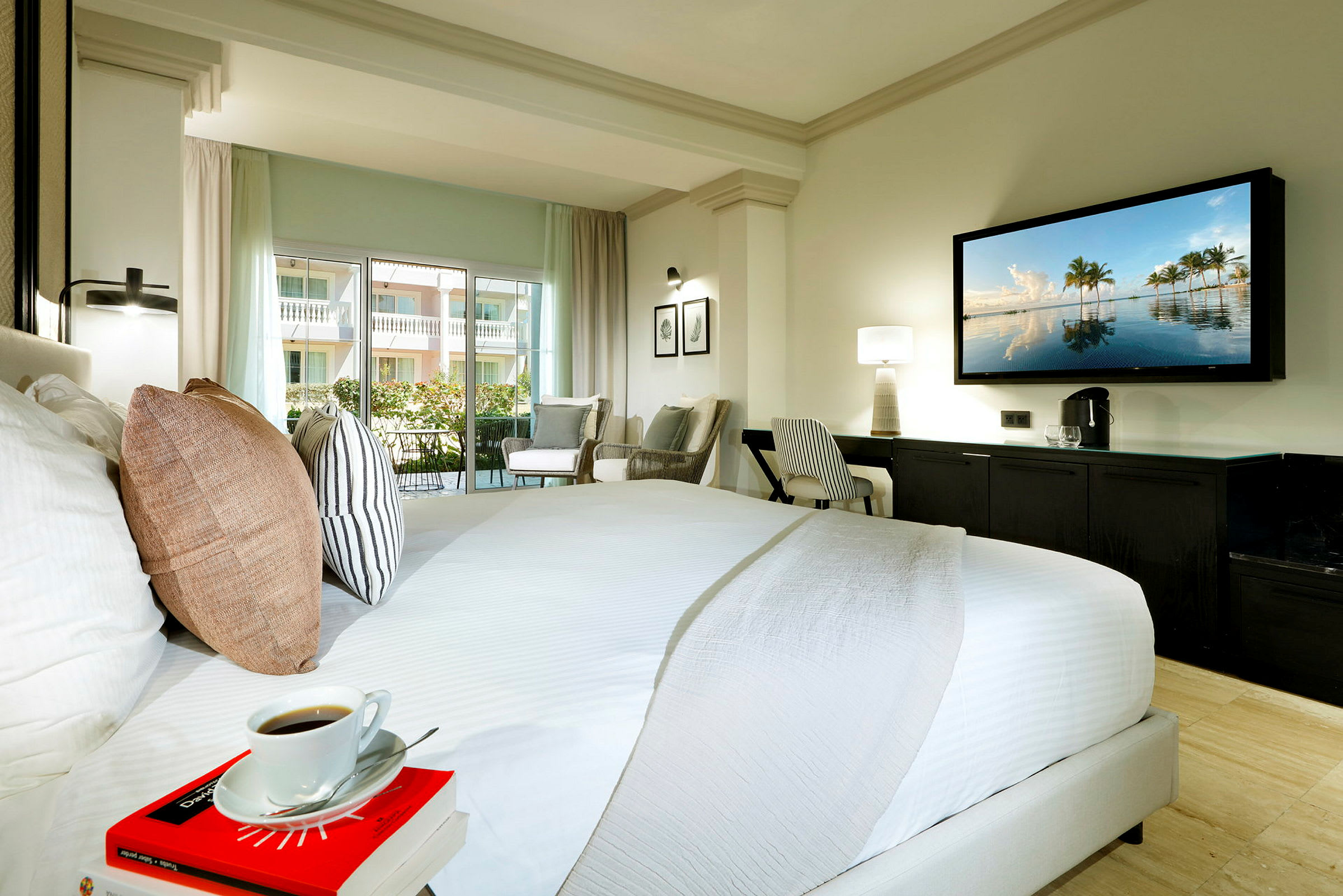 Hotellrum med stor säng, sittgrupp, skrivbord och TV på väggen. (AI-genererad text)