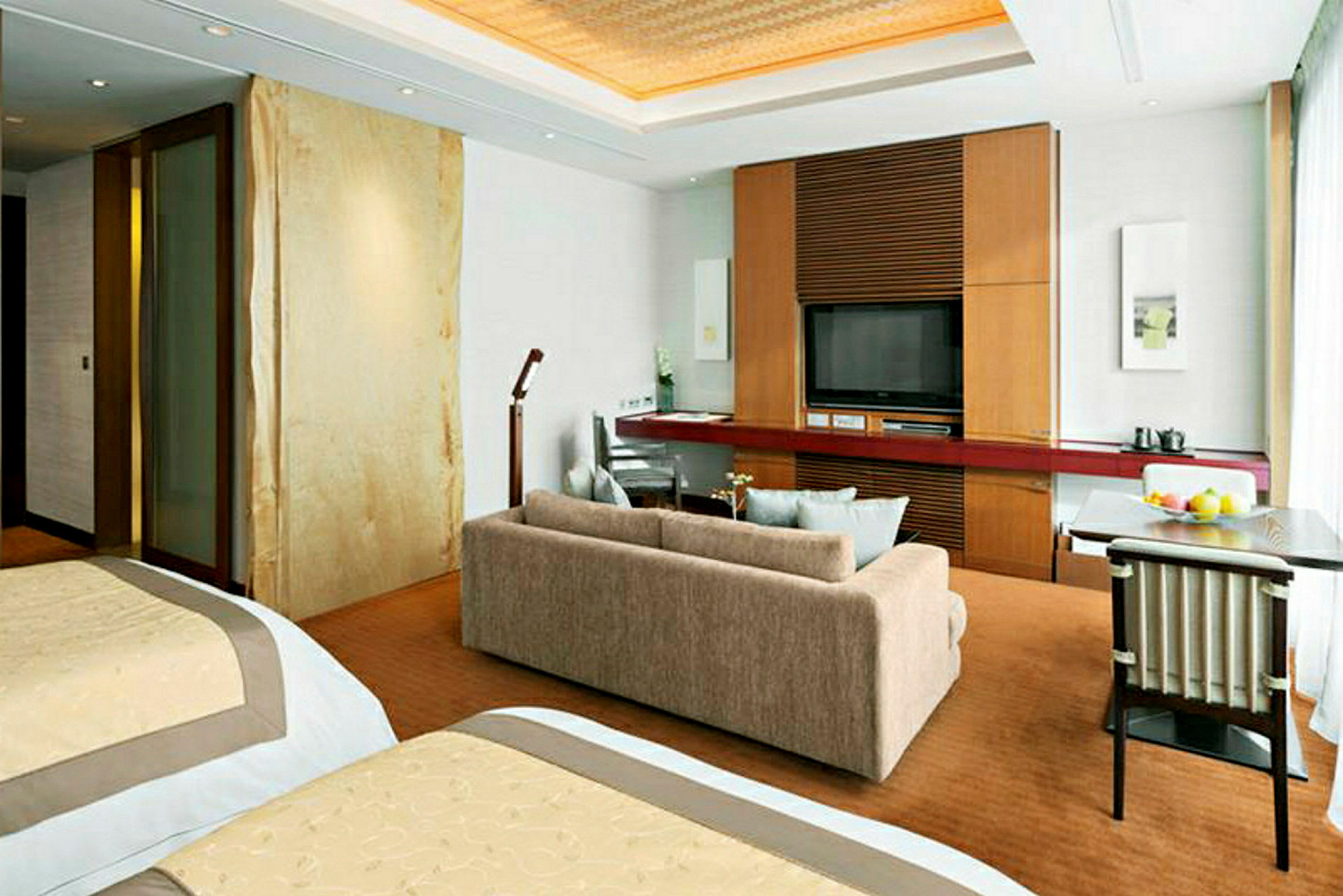 Ett hotellrum med två sängar, soffa, ett skrivbord och en TV på en träpanel. (AI-genererad text)