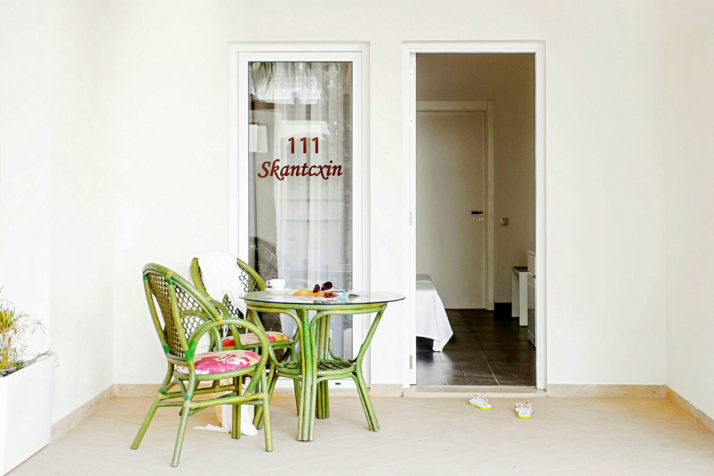 Grön bord och stolar på en terrass utanför ett hotellrum med öppet dörr. (AI-genererad text)