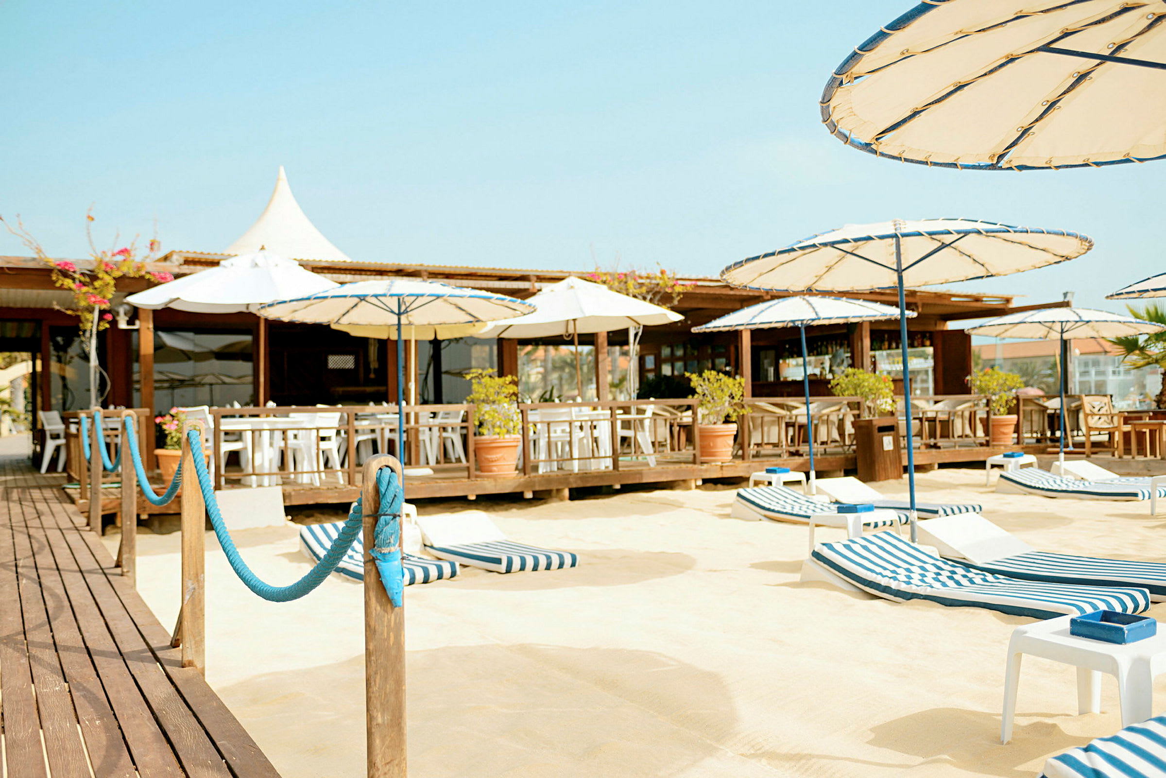 En strandbar med sittplatser, parasoller och solstolar på en sandig yta. (AI-genererad text)