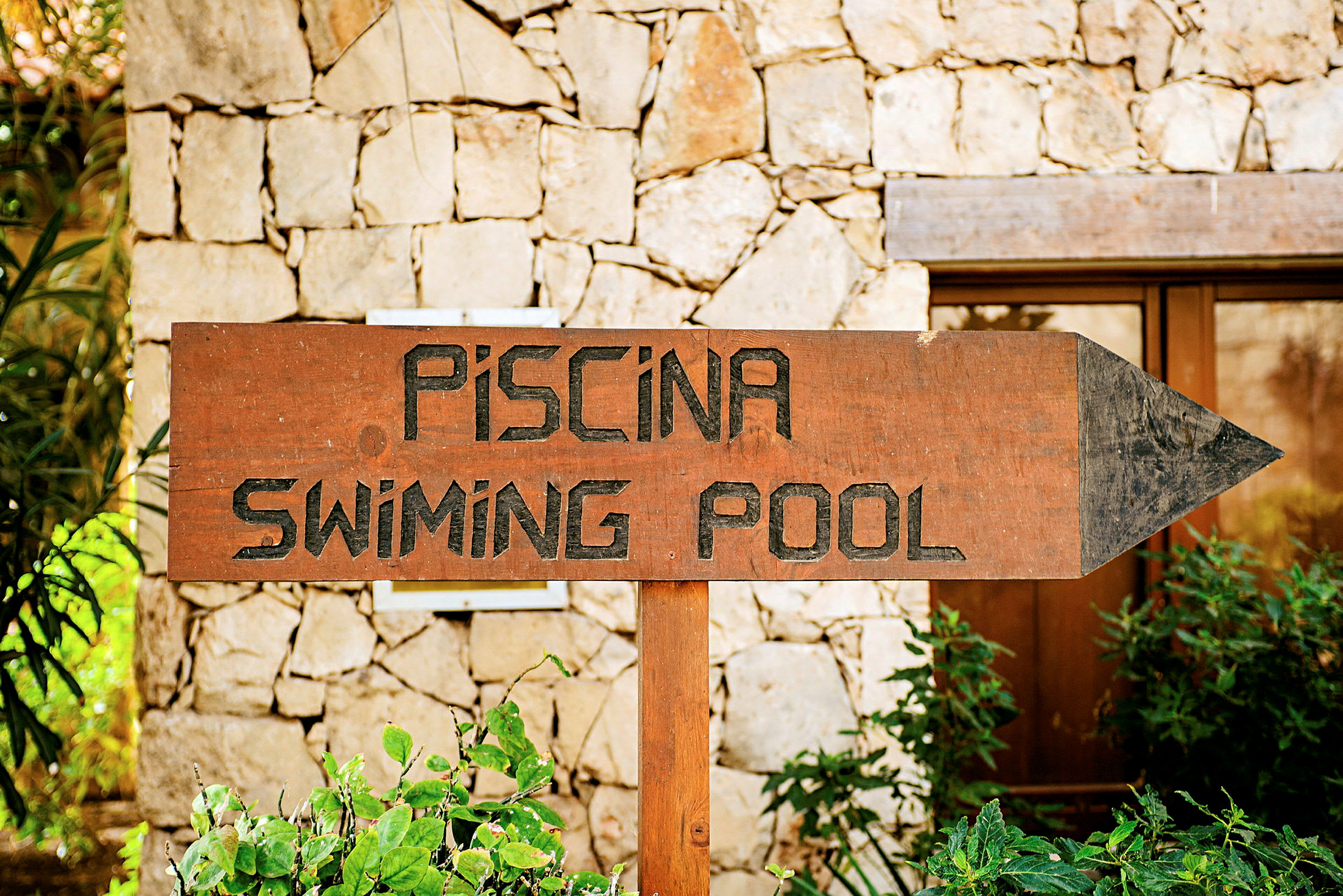 Skylt med texten 'Piscina - Swimming Pool' framför stenmur. (AI-genererad text)