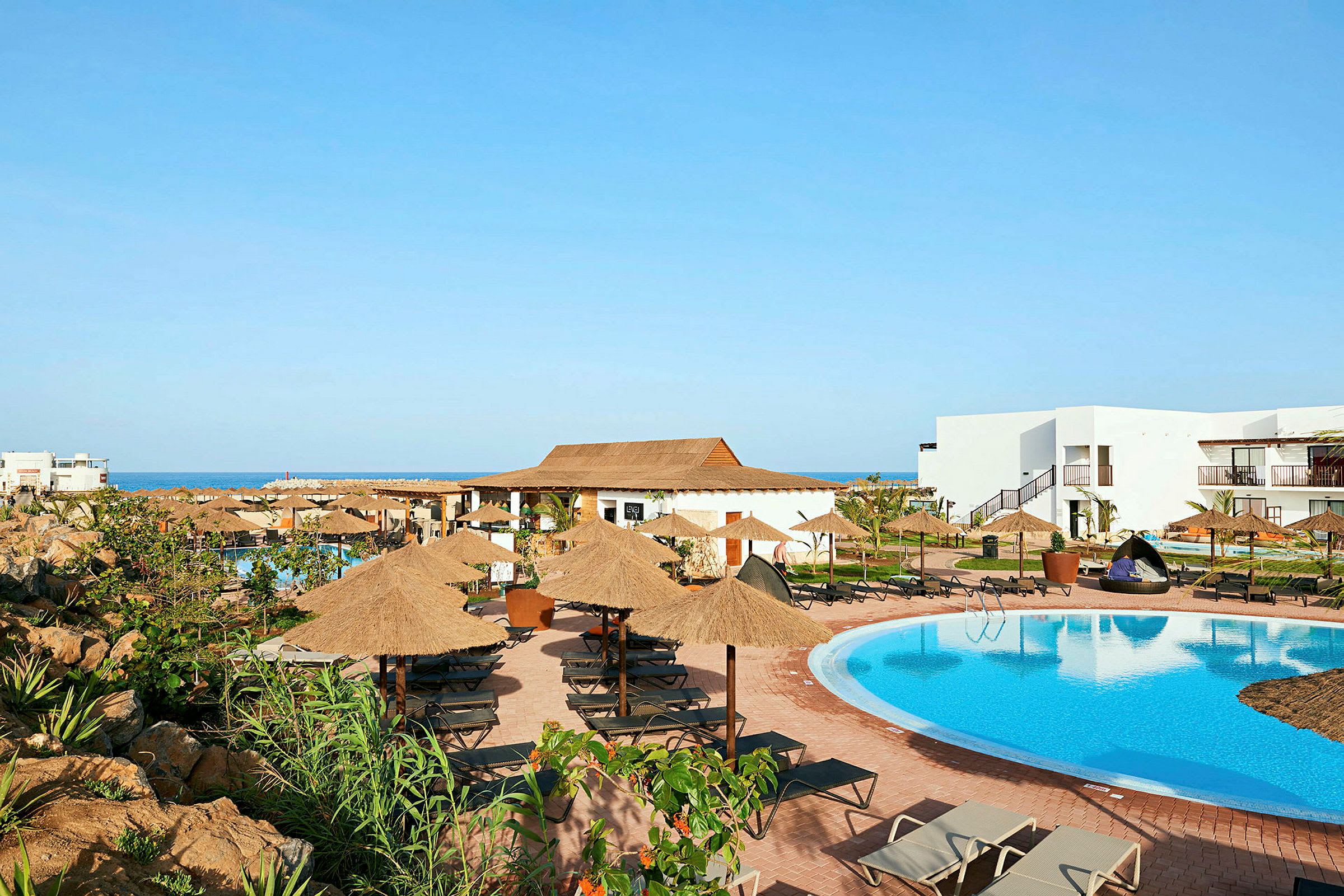 En hotellpool med solstolar och parasoller omgivna av byggnader. (AI-genererad text)
