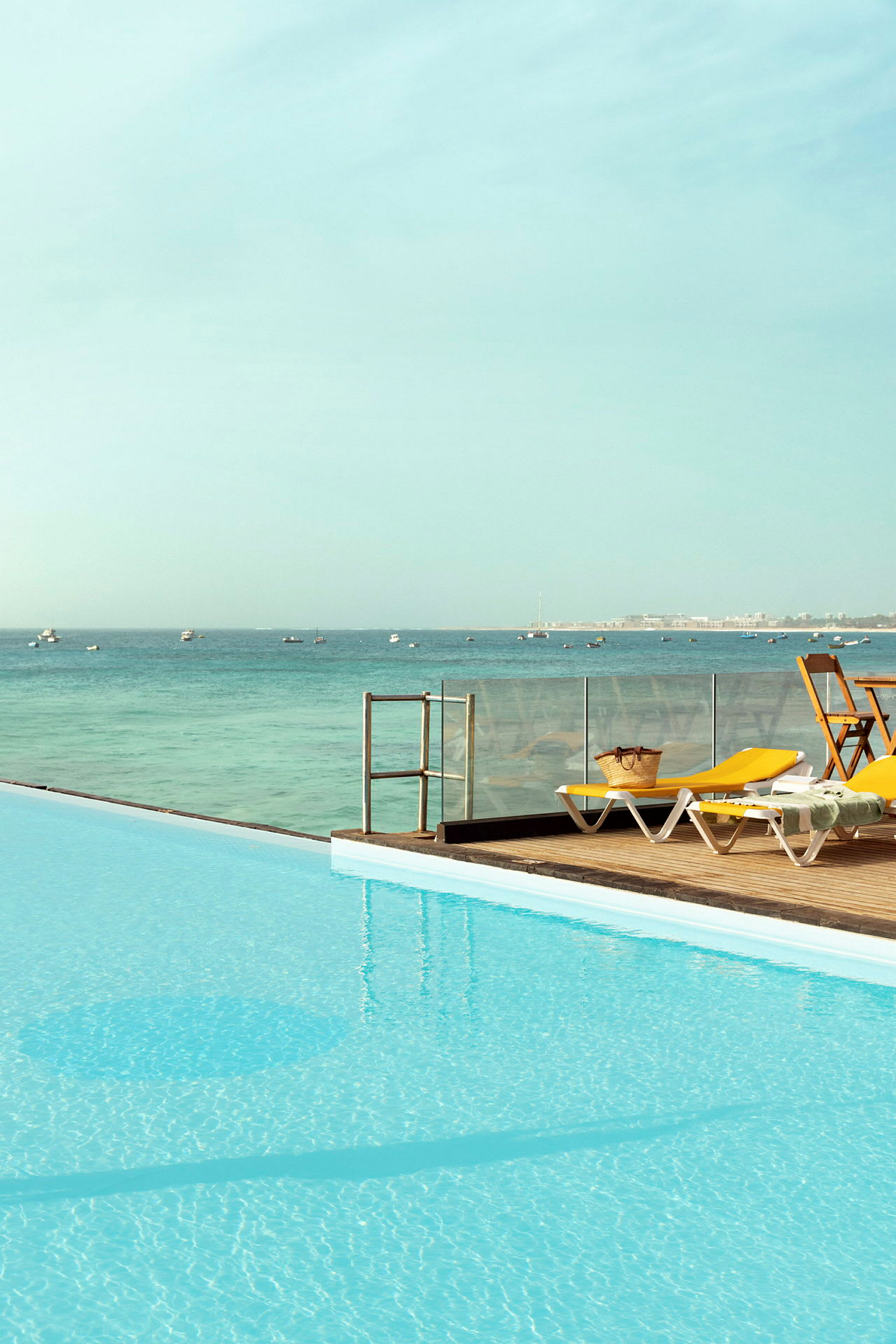 Pool med utsikt över havet. Solstolar och bord med stolar på terrassen. (AI-genererad text)