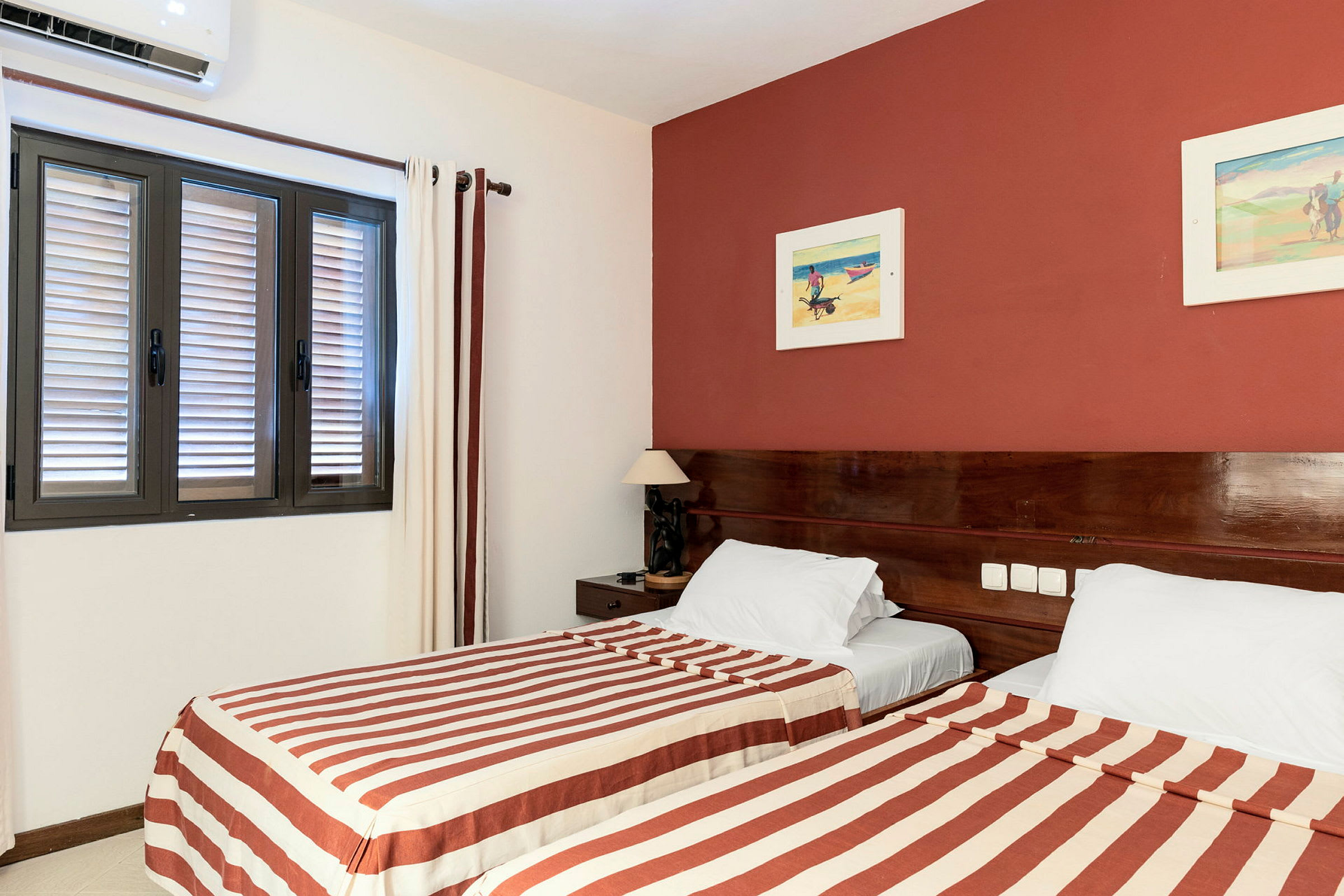 Ett hotellrum med två enkelsängar med randiga sängkläder och en vägg med rödmålning. (AI-genererad text)