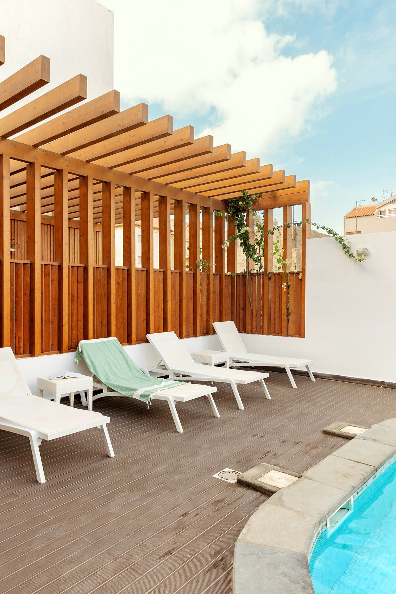 Solsängar på en terrass vid en pool med trägolv och pergola. (AI-genererad text)