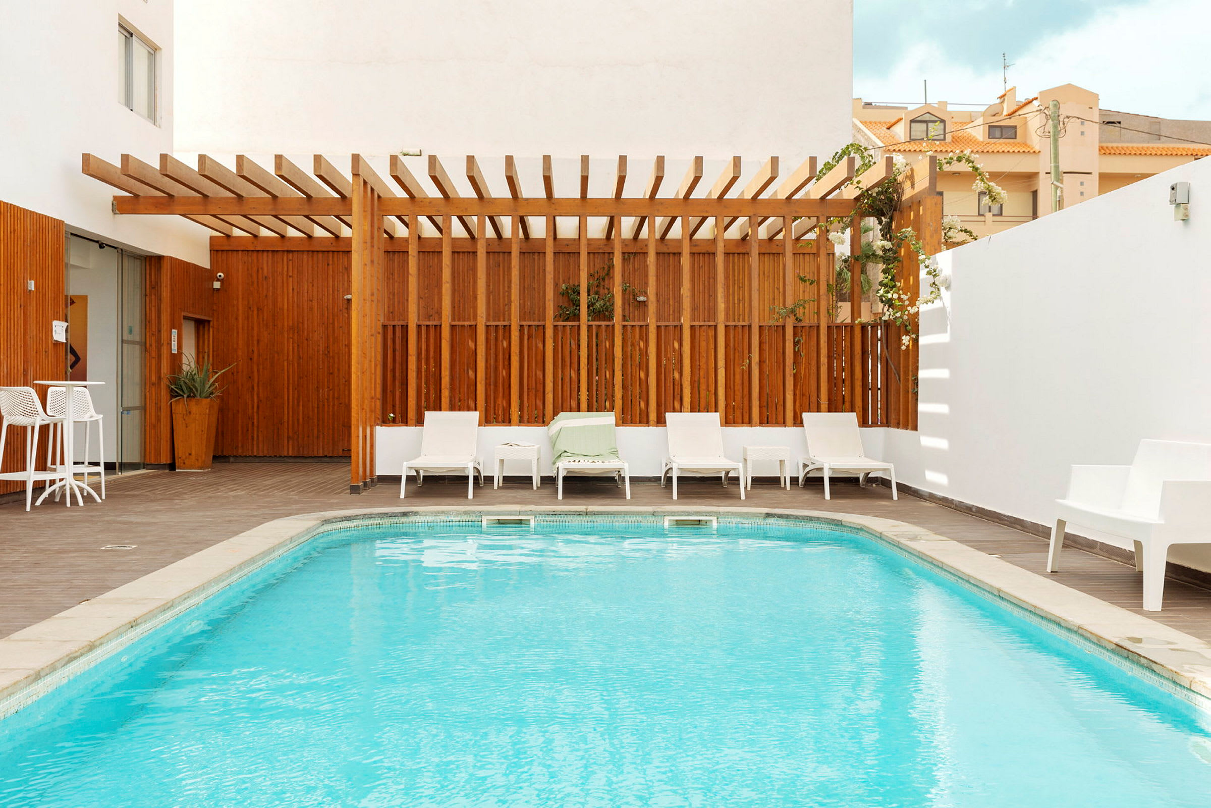 En liten pool med omgivande solstolar och trädäck, en träram skapar en avskild atmosfär. (AI-genererad text)