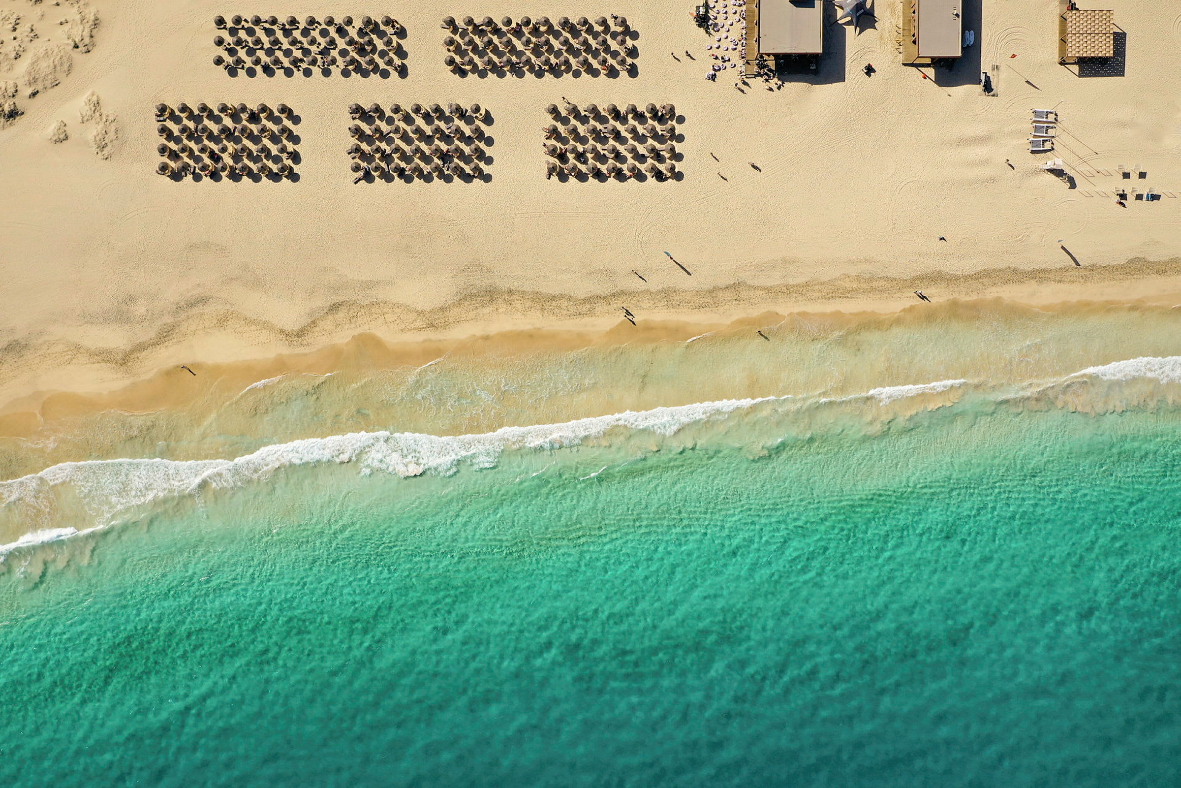 Flygfoto över en strand med parasoller, sand och havsvågor. (AI-genererad text)