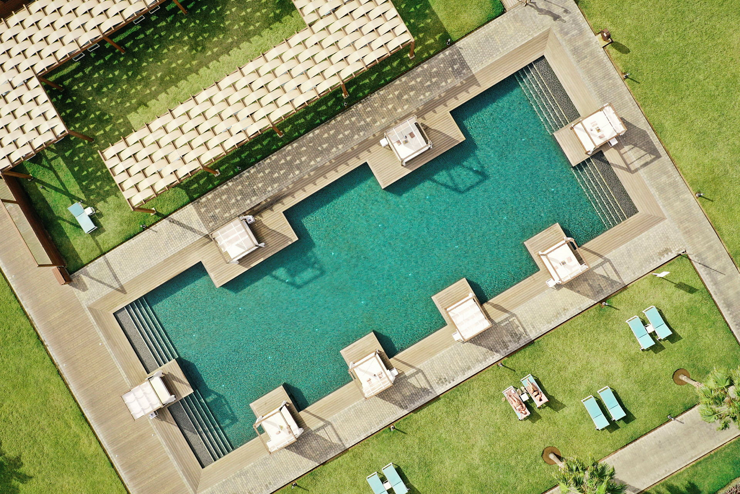 Vy ovanifrån av en pool med solstolar och gröna gräsytor omkring. (AI-genererad text)