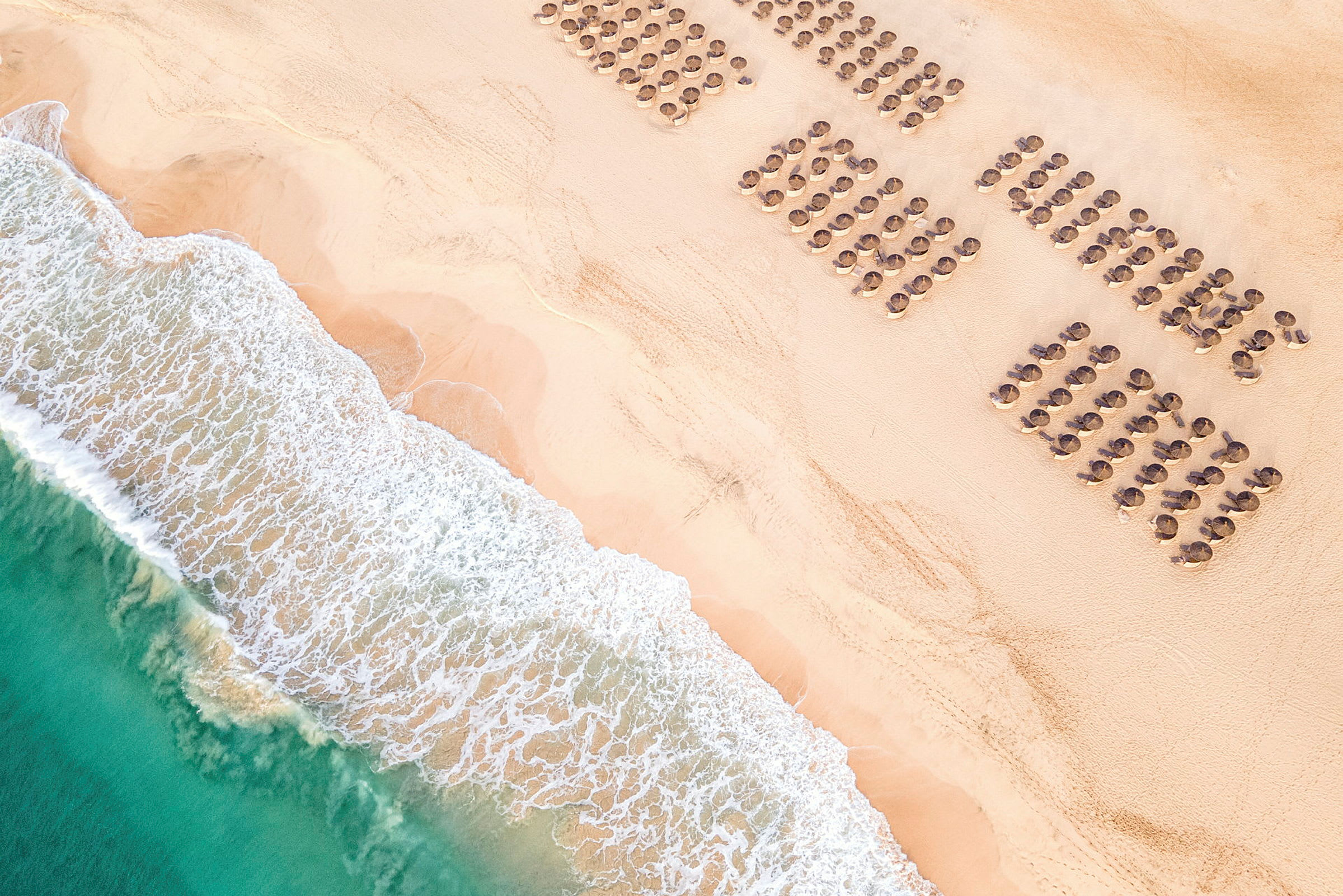 Flygbild av en strand med parasoller i rader och vågor som når land. (AI-genererad text)