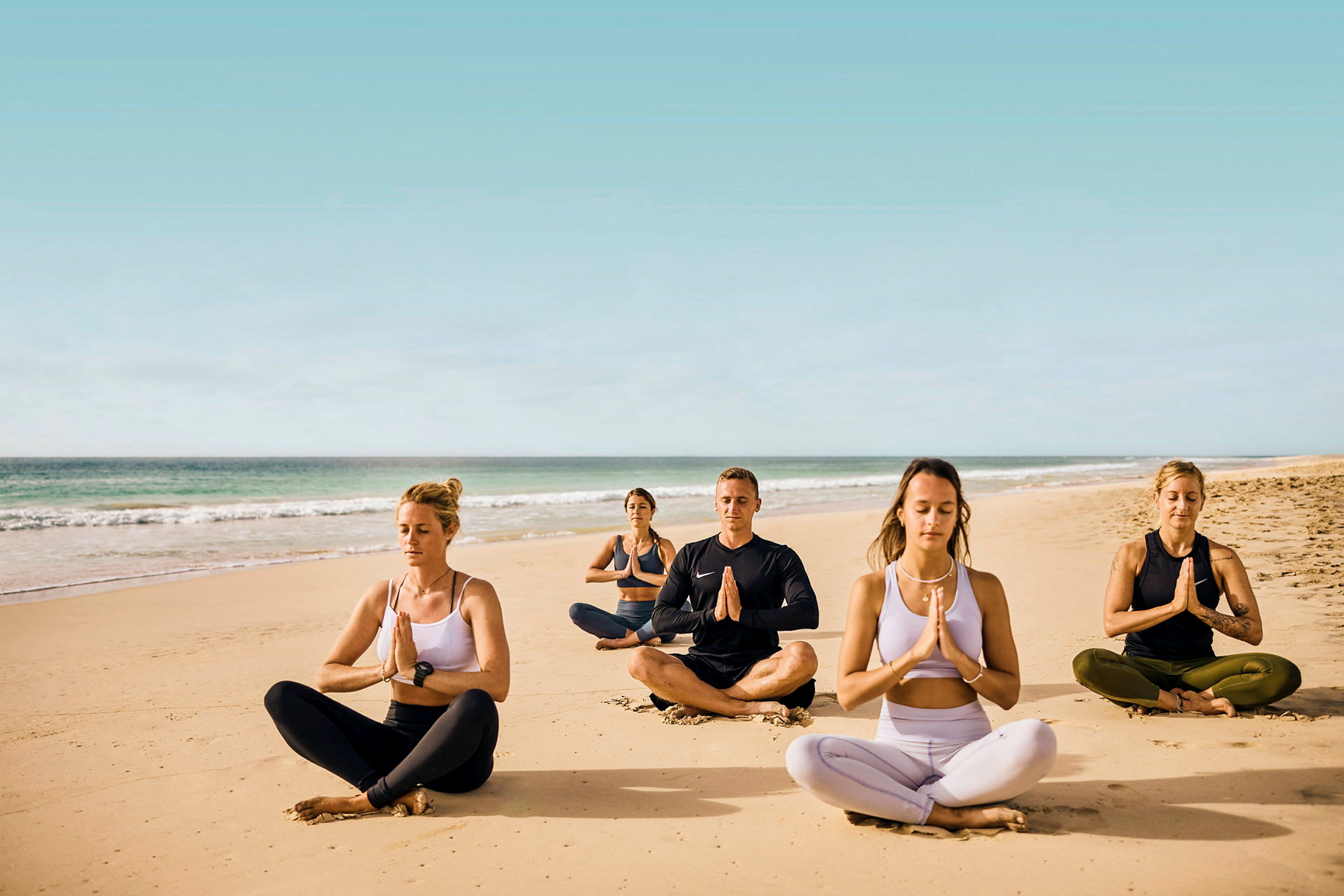 En grupp människor som utövar meditation på en sandstrand. (AI-genererad text)