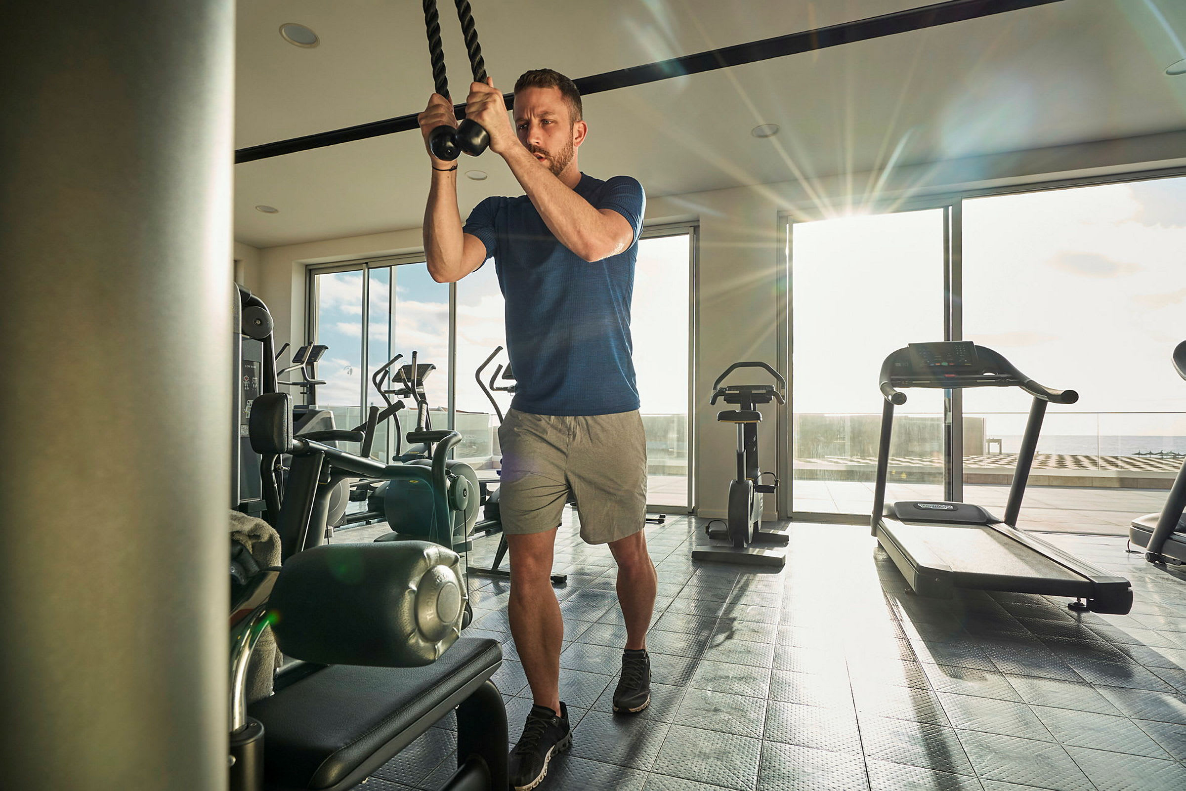 Person tränar med rep i ett gym med utsikt över en solig terrass. (AI-genererad text)