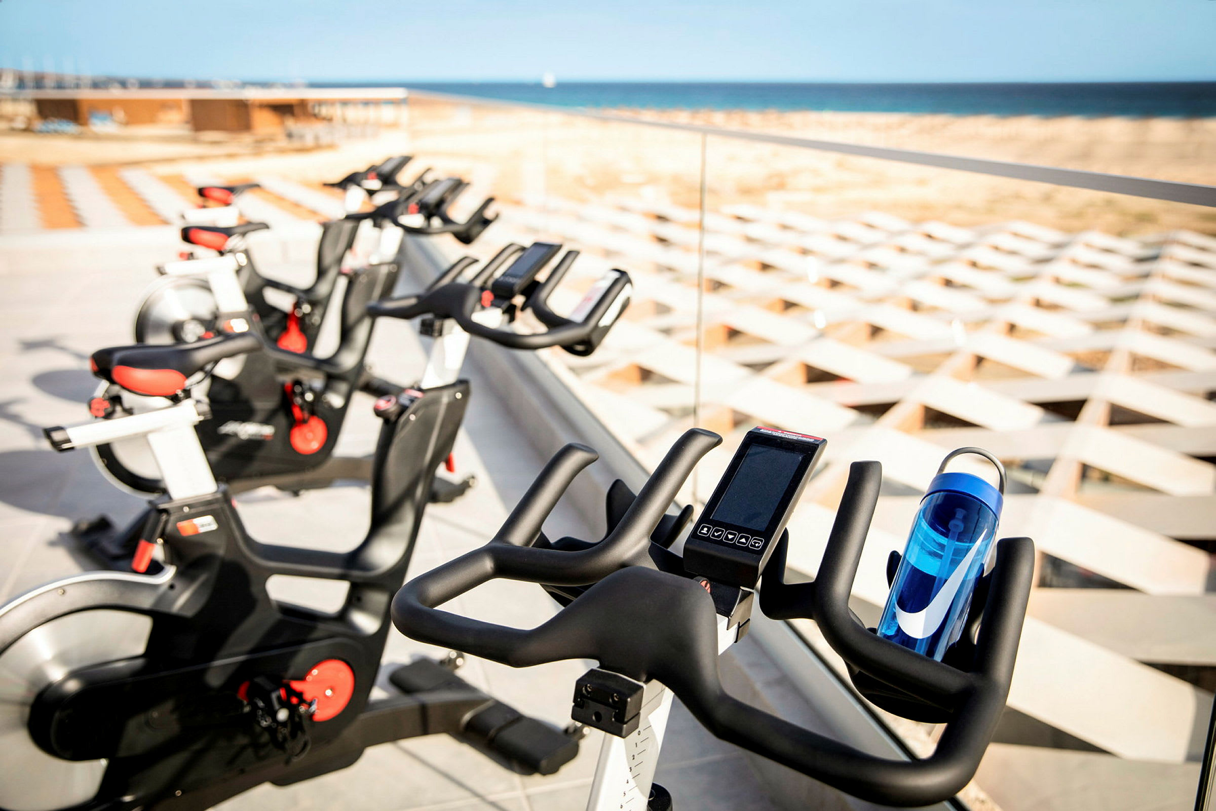 Bild av flera träningscyklar placerade vid ett glasräcke med utsikt över stranden och havet. (AI-genererad text)