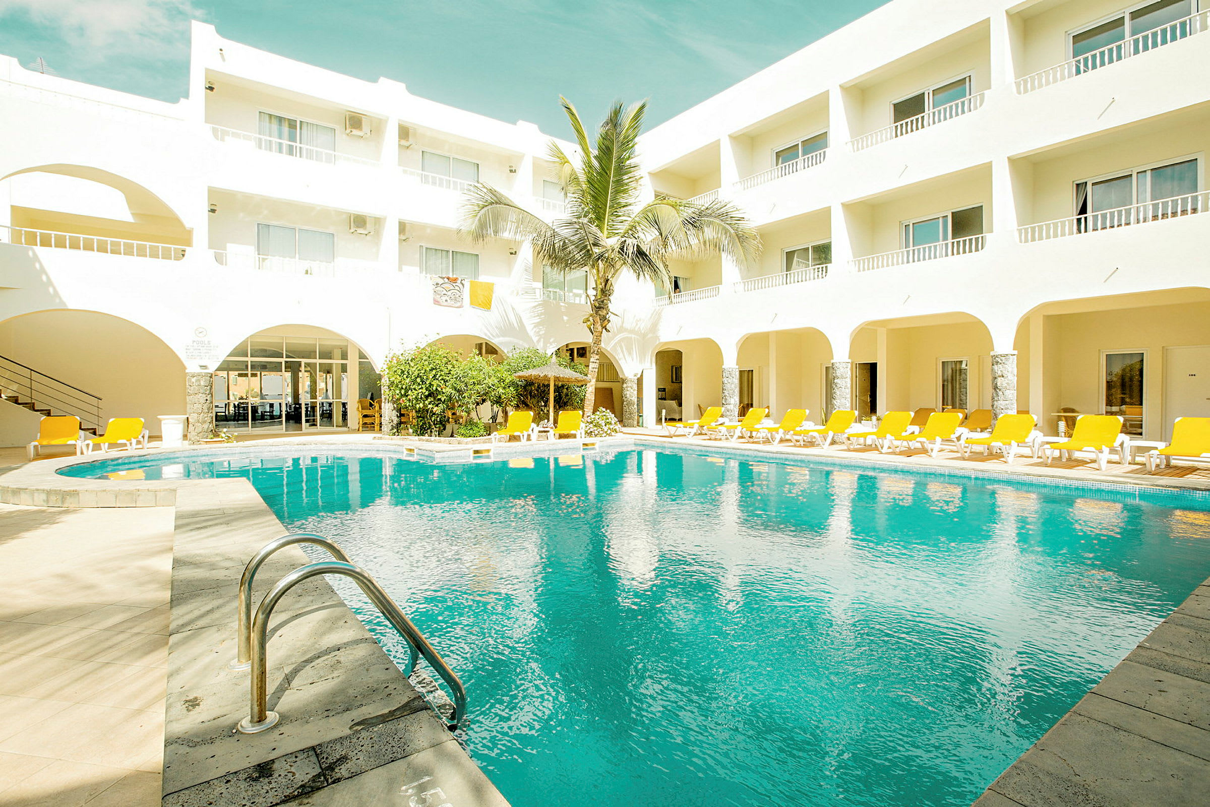 Hotellbyggnad med en pool och solstolar runt omkring. (AI-genererad text)