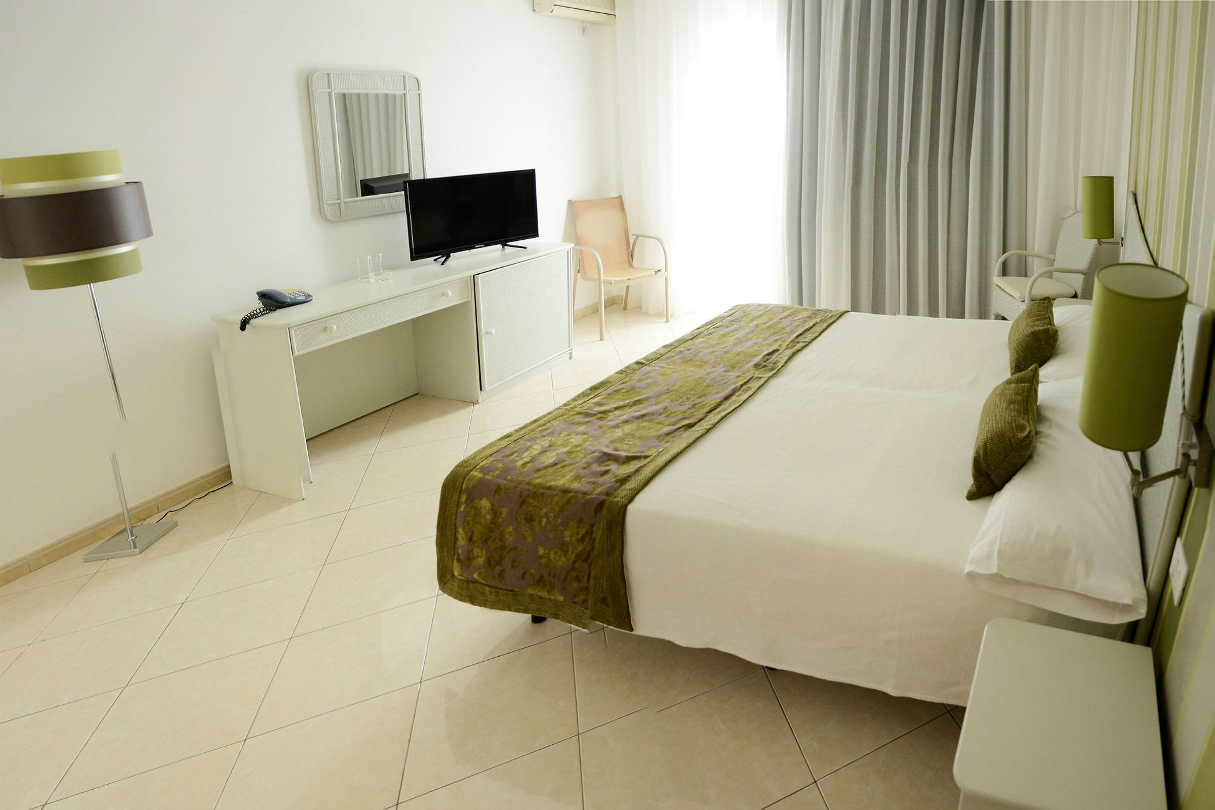 Hotellrum med en dubbelsäng, skrivbord med spegel och TV, samt en lamparmatur. (AI-genererad text)