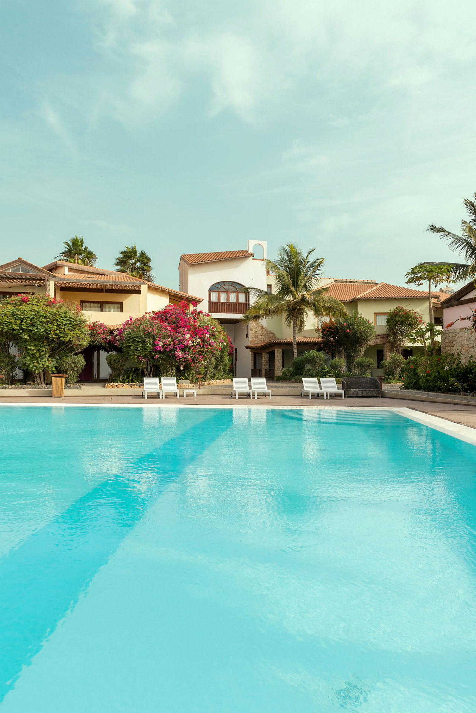 Utomhuspool vid ett semesterhotell med solsängar och grönskande omgivning. (AI-genererad text)