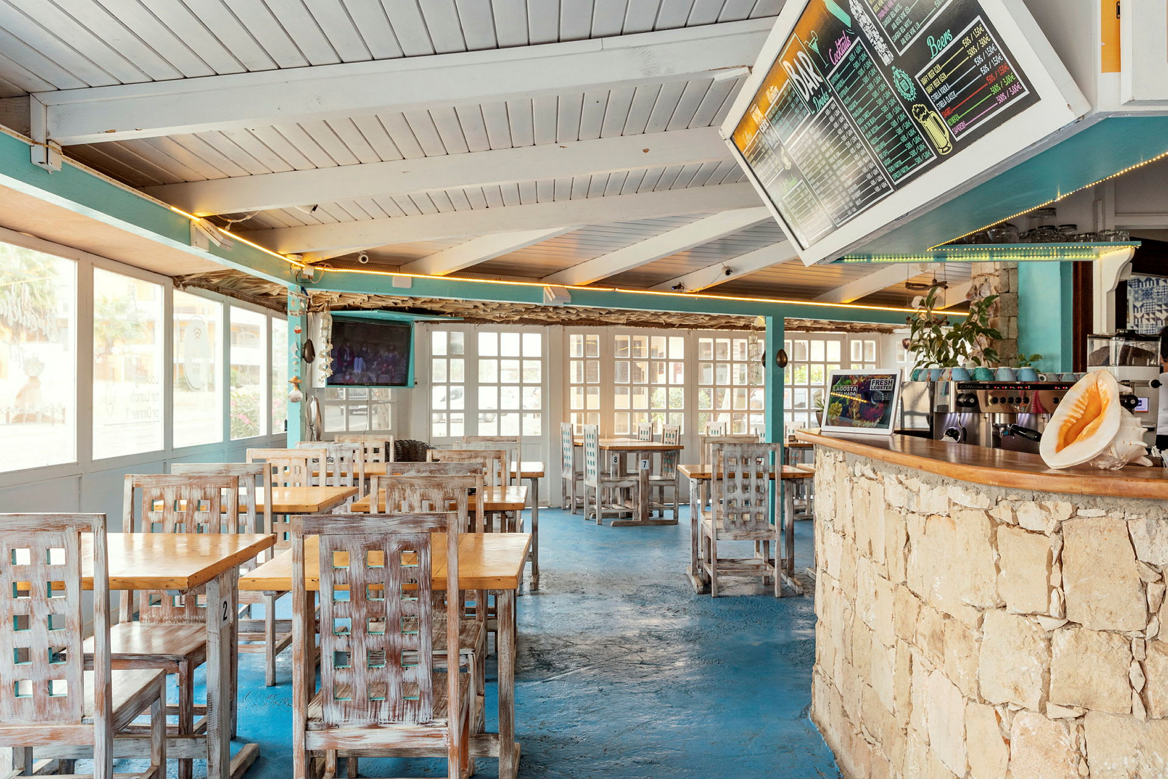 Interiör av en restaurang med träbord och stolar, blå golv, och en meny på väggen. (AI-genererad text)