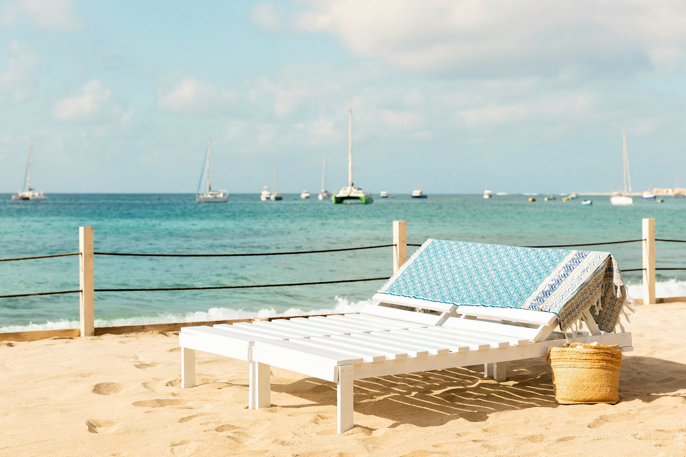 Vit solstol med blå handduk på strand med hav i bakgrunden. (AI-genererad text)