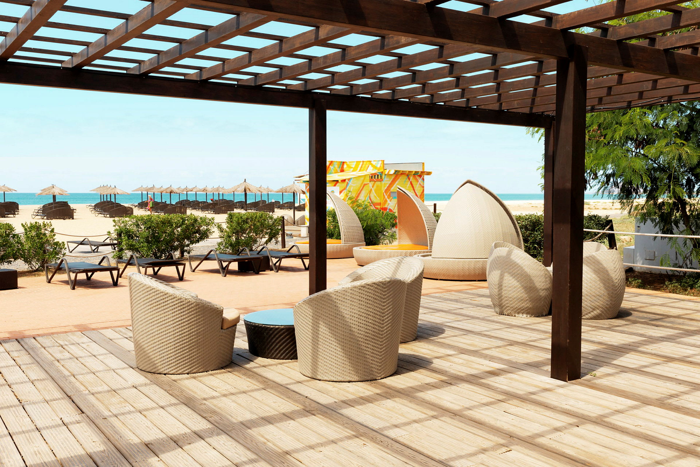 Loungeområde med sittmöbler under en pergola nära stranden. (AI-genererad text)