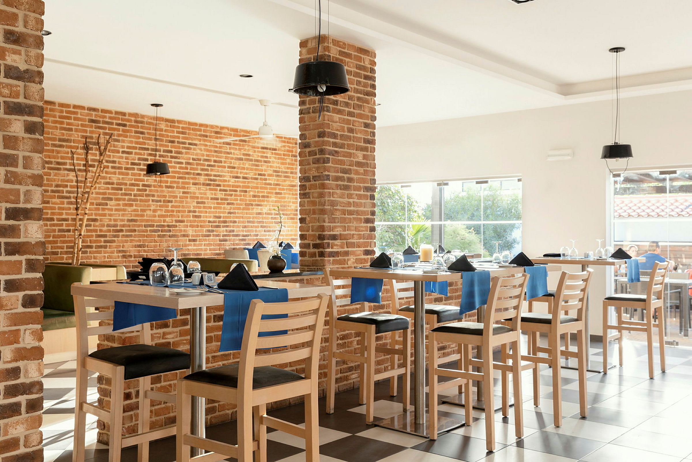 Interiör av en restaurang med brickväggar, fullt möblerad med bord och stolar dekorerade med blå detaljer. (AI-genererad text)
