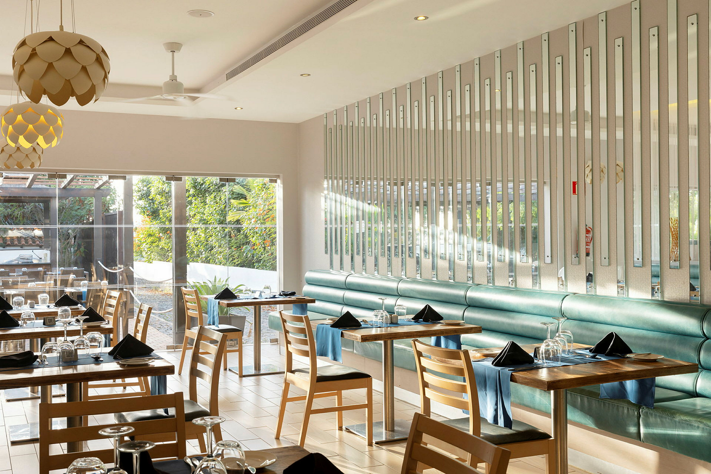 Ett modernt och ljusrestauranginteriör med bord och stolar, där fönster vetter mot ett grönskande utomhusområde. (AI-genererad text)