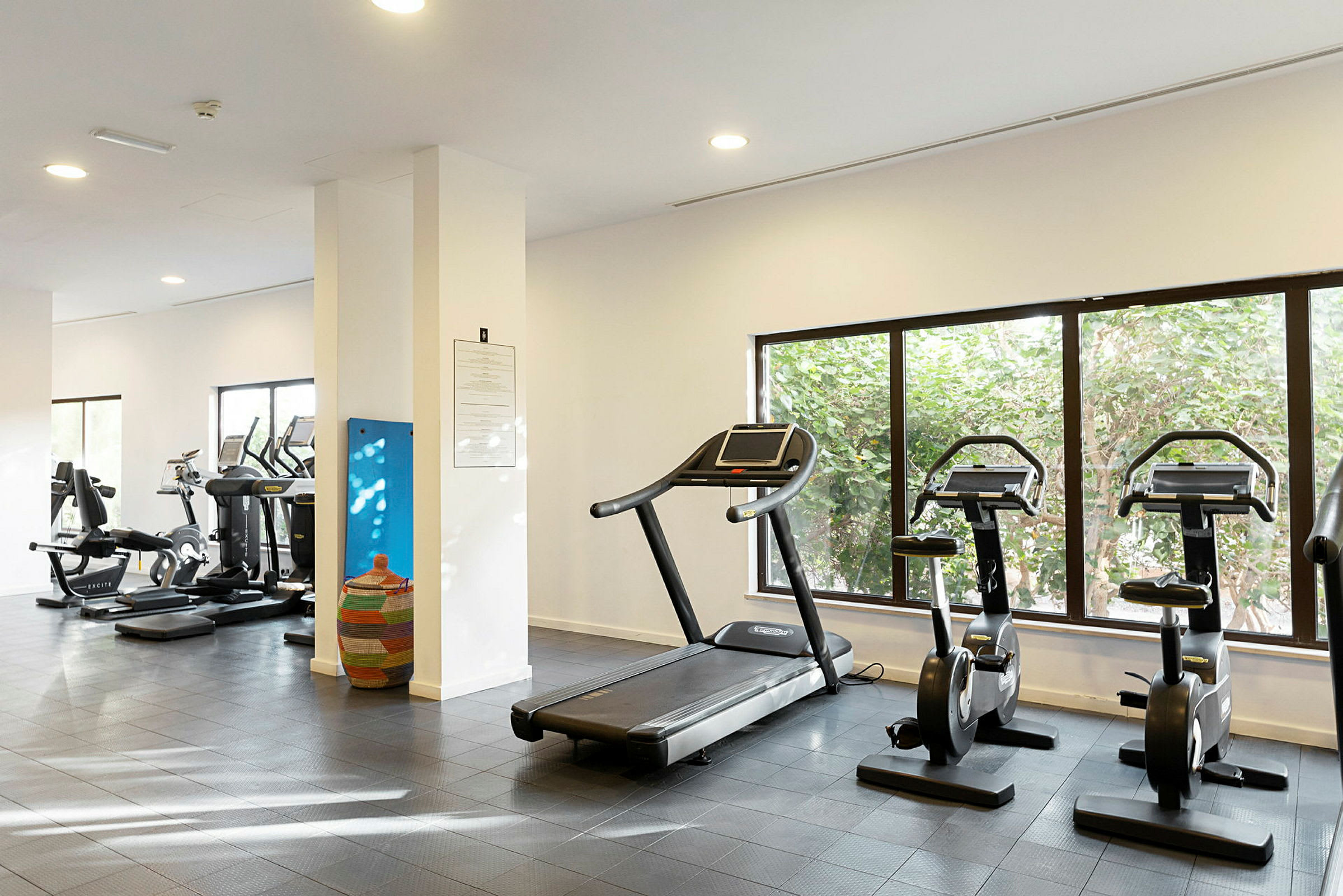 Ett gym med träningsmaskiner, inklusive löpband och motionscyklar, bredvid fönster. (AI-genererad text)