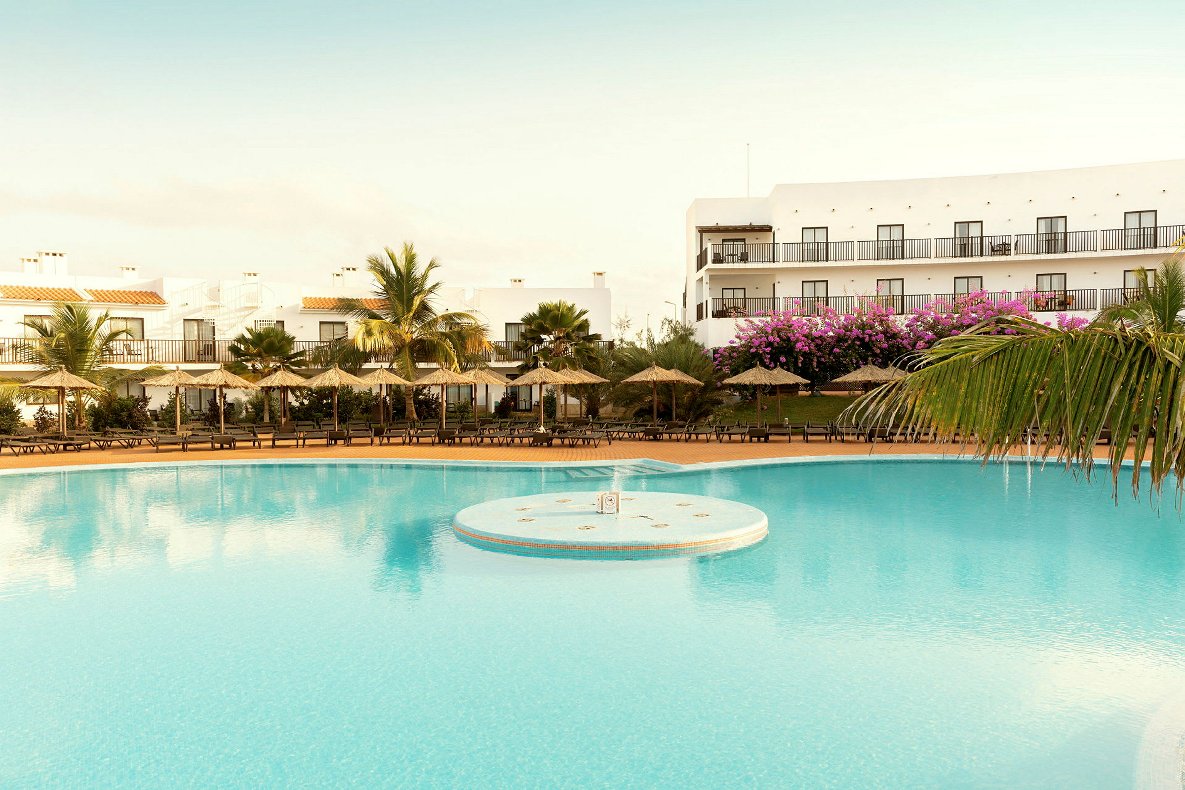 Bild av en pool vid en resort med parasoller och byggnader i bakgrunden. (AI-genererad text)