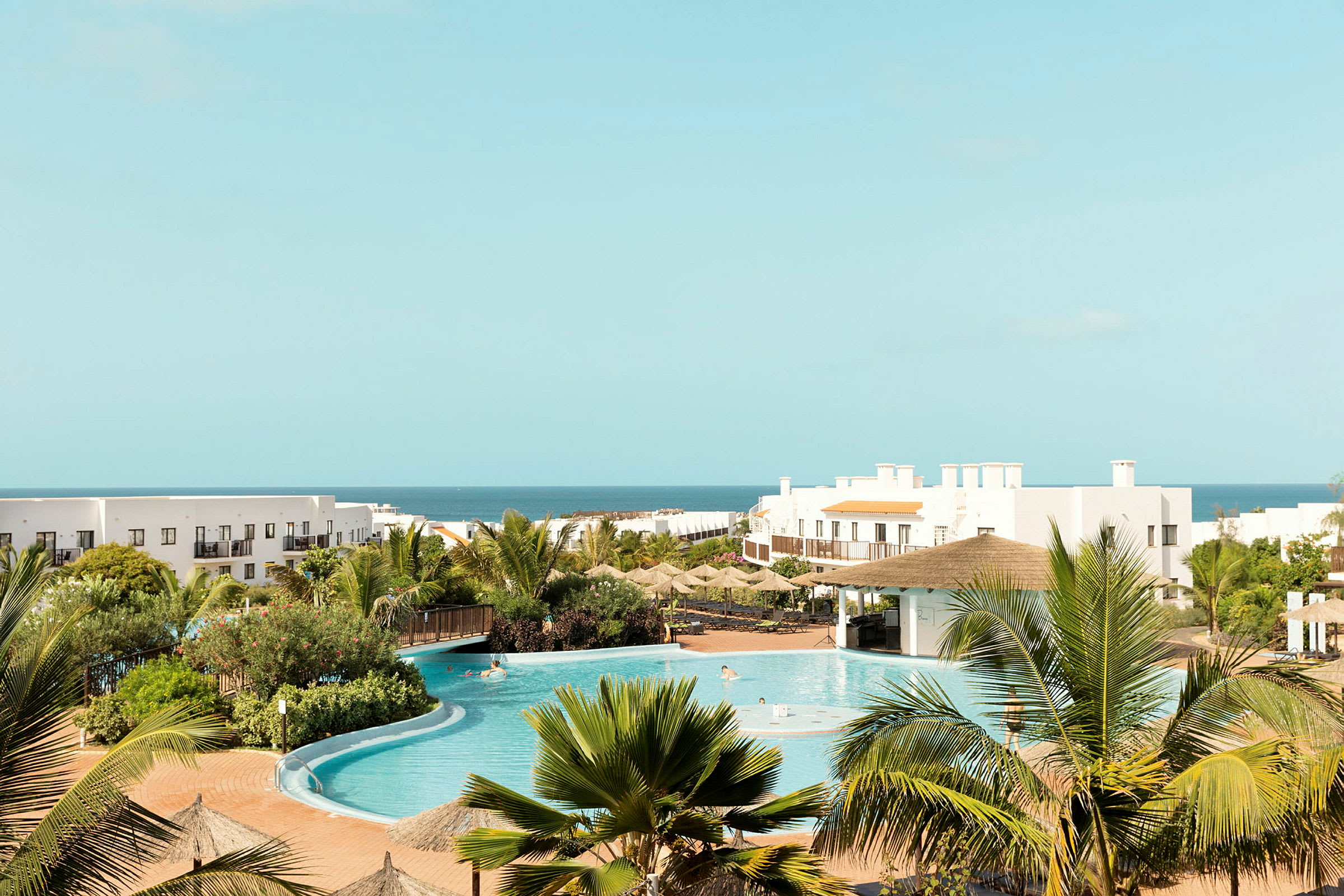 Hotellanläggning med pool, grönska och hav i bakgrunden. (AI-genererad text)