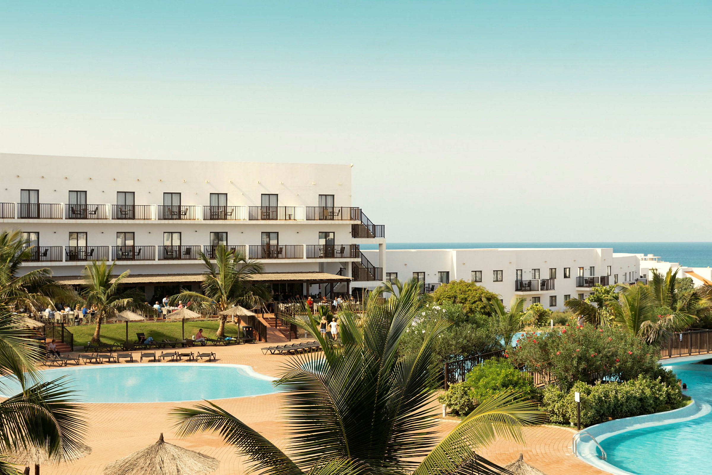 Hotellbyggnad vid en pool och grönska. (AI-genererad text)