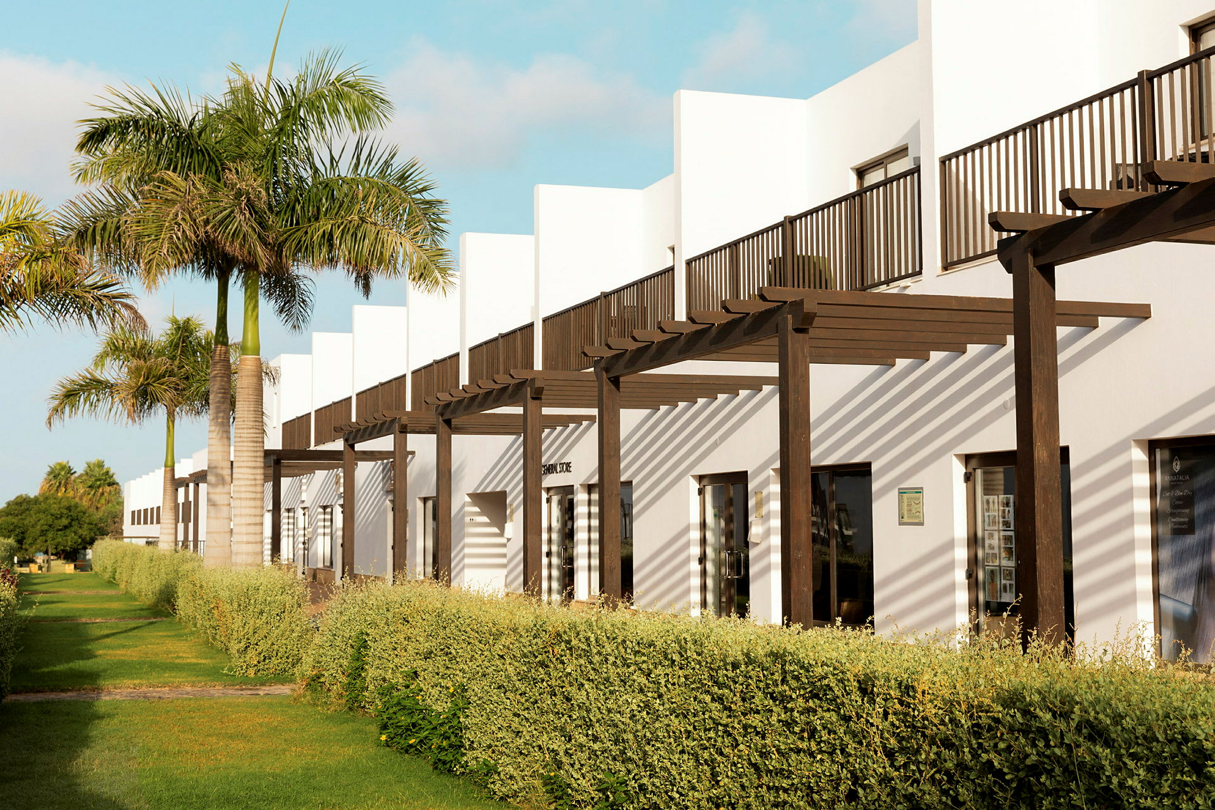 Exteriör av en rad moderna vita byggnader med träpergola och omgivande grönska. (AI-genererad text)
