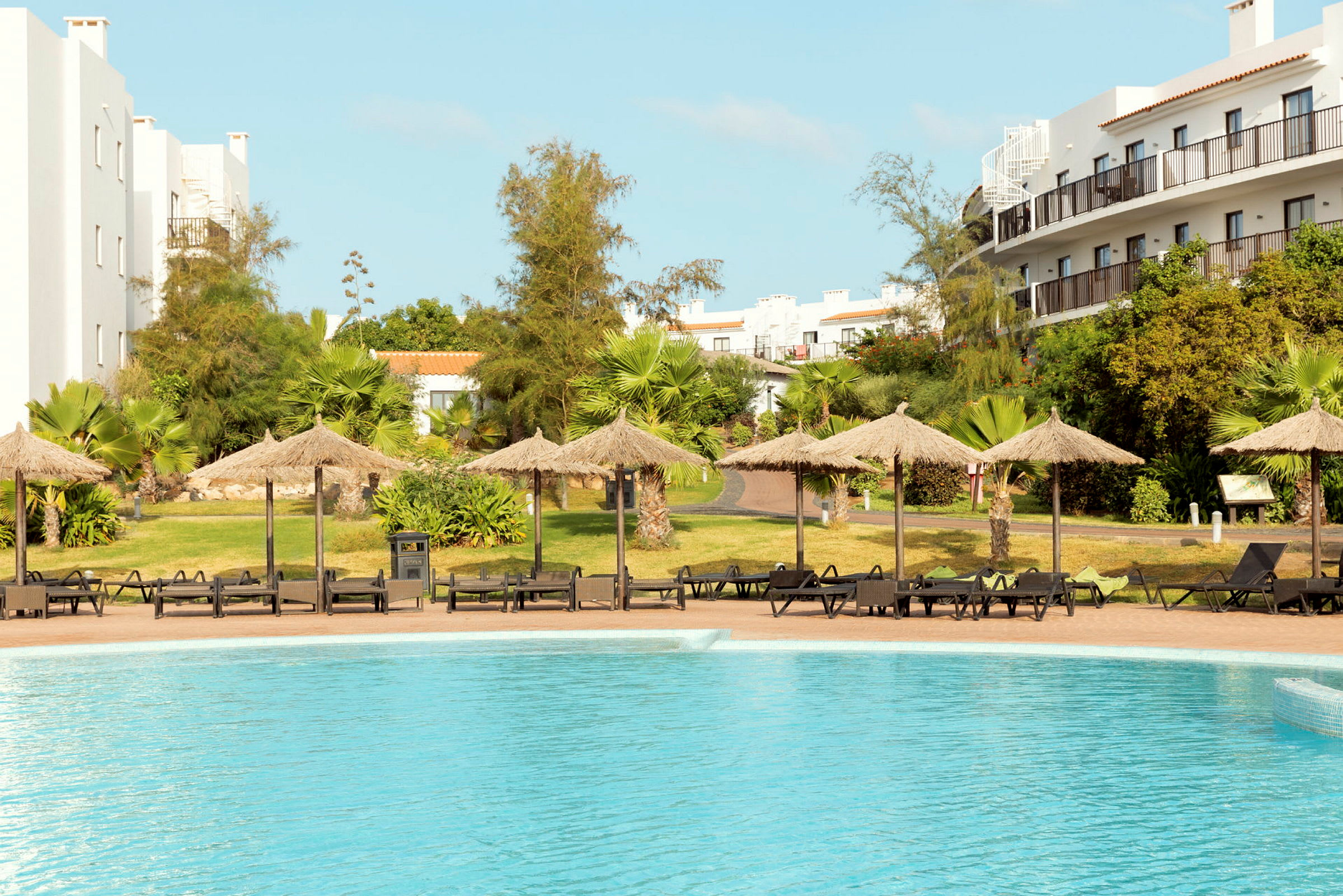 Pool med parasoll och solstolar vid hotellområde. (AI-genererad text)