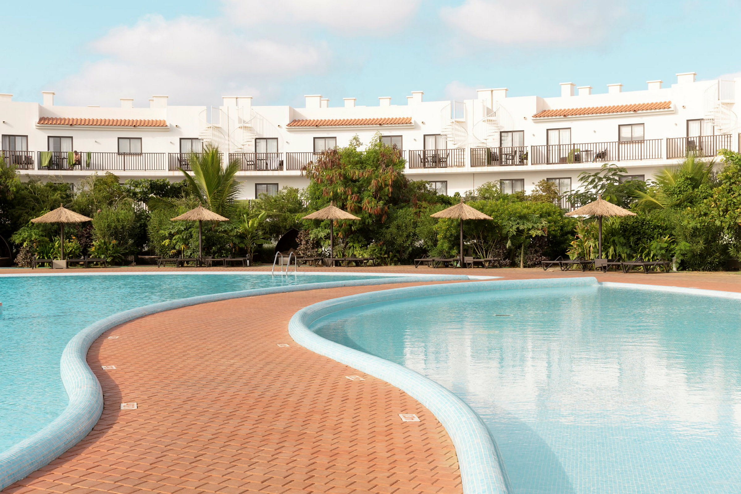En hotellpool med parasoller och grönska i bakgrunden. (AI-genererad text)