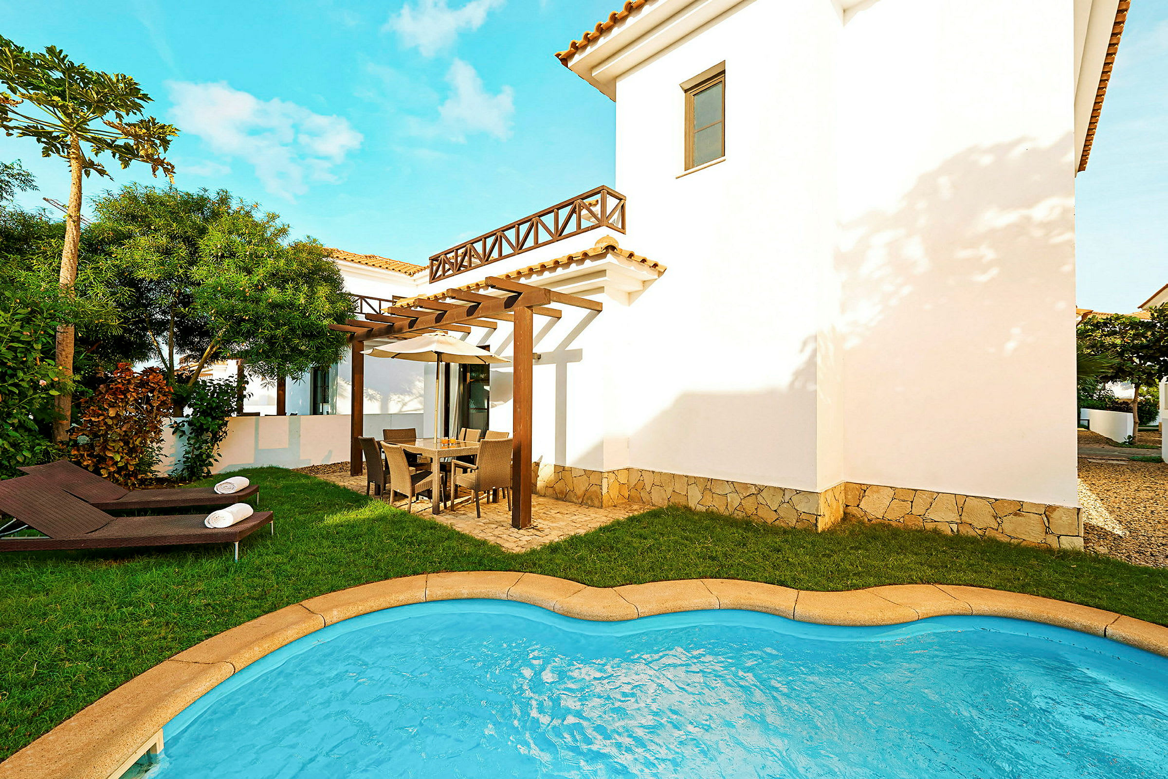 Bild av en villa med en liten pool, gräsmatta och utemöbler på en rymlig terrass. (AI-genererad text)