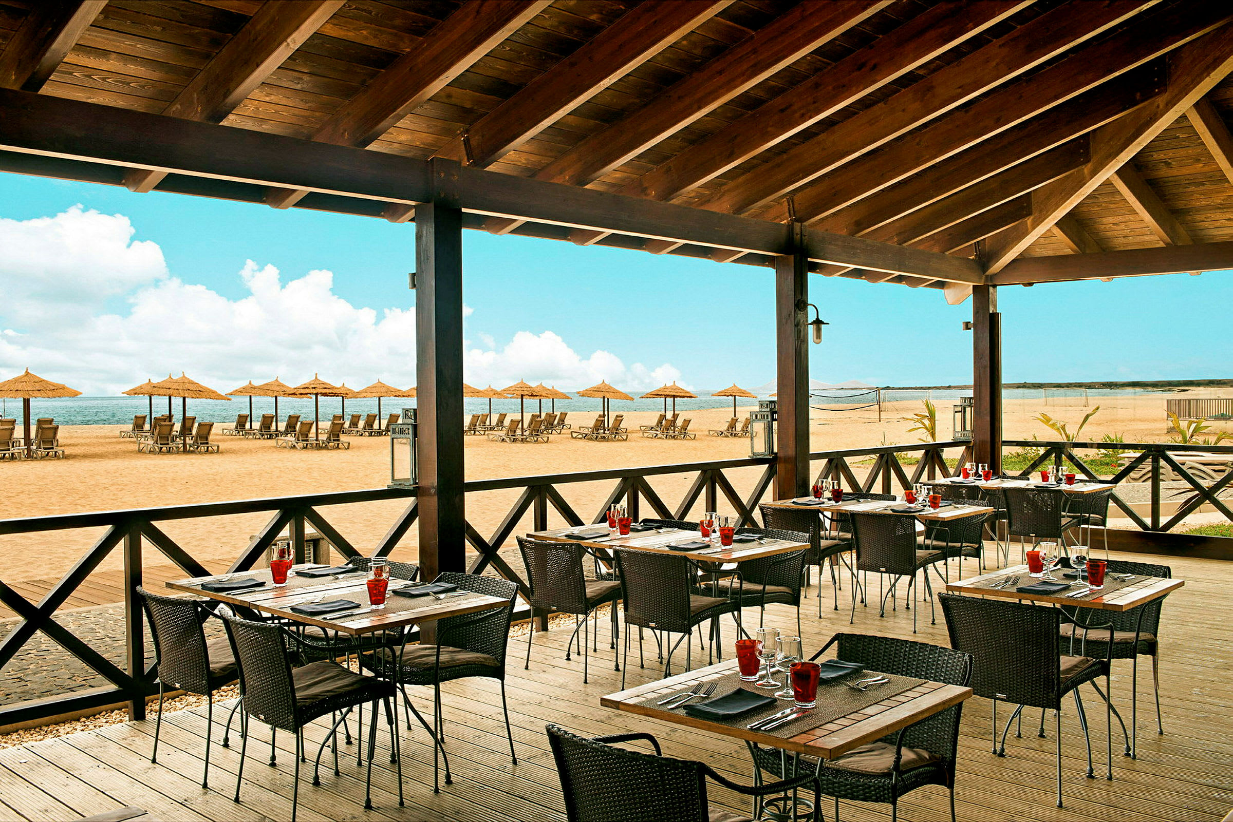 Restaurang med uteservering och utsikt över en strand med solstolar och parasoller. (AI-genererad text)