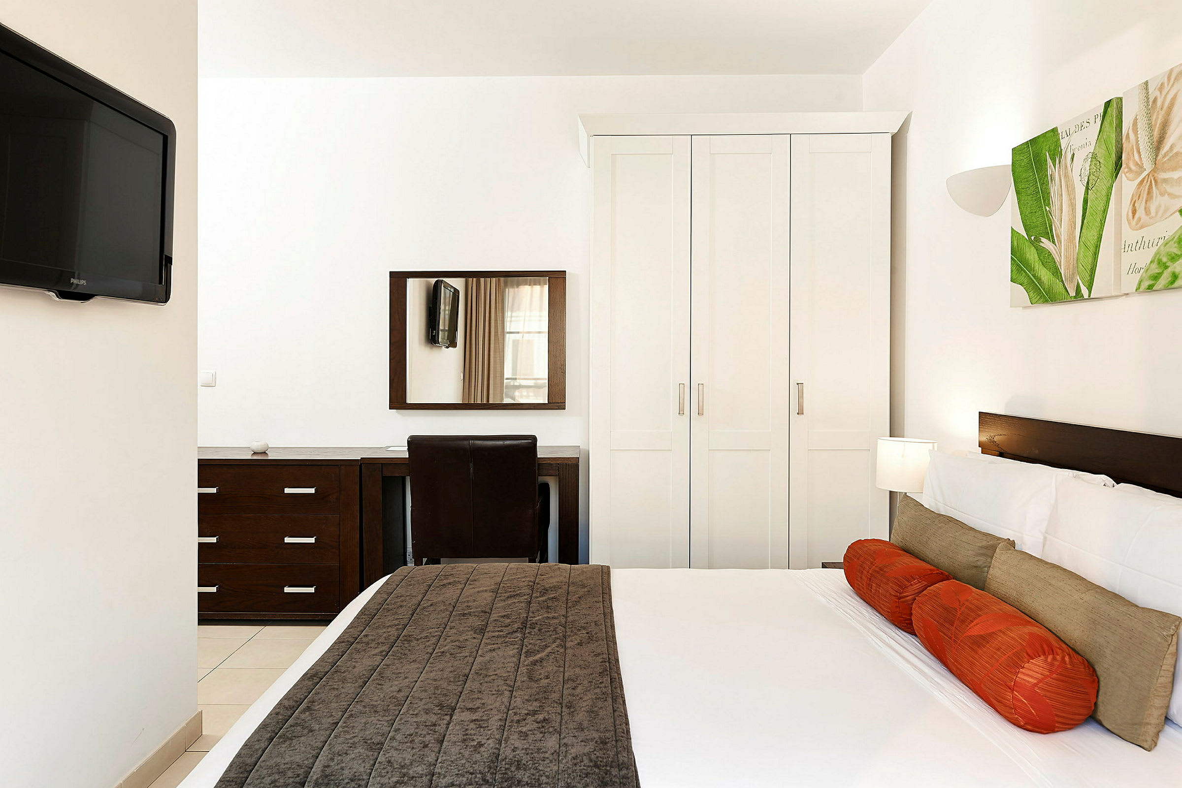 Ett hotellrum med en säng, garderob, spegel och TV. (AI-genererad text)